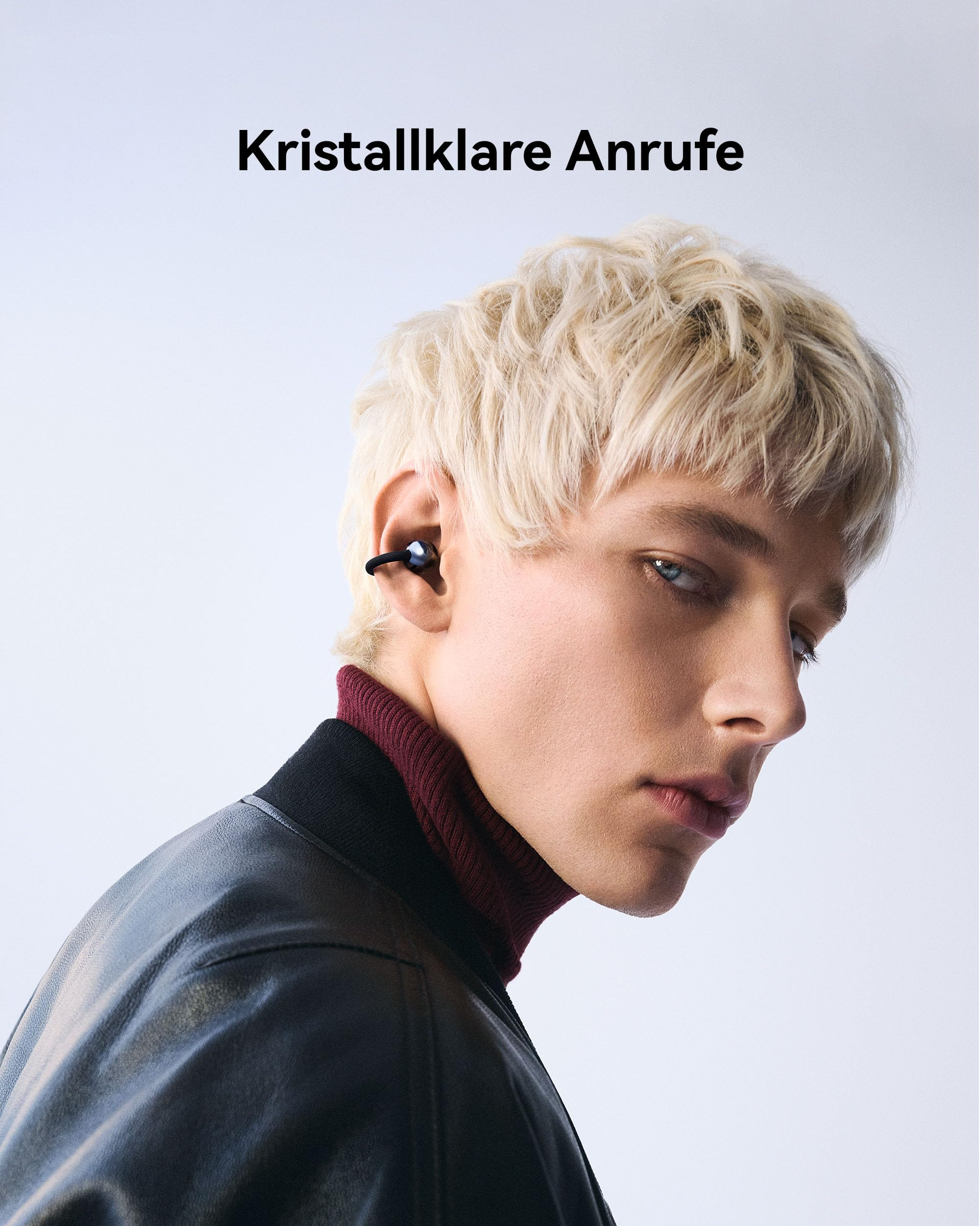 Un uomo biondo con giacca di pelle nera e dolcevita rosso che indossa auricolari wireless.