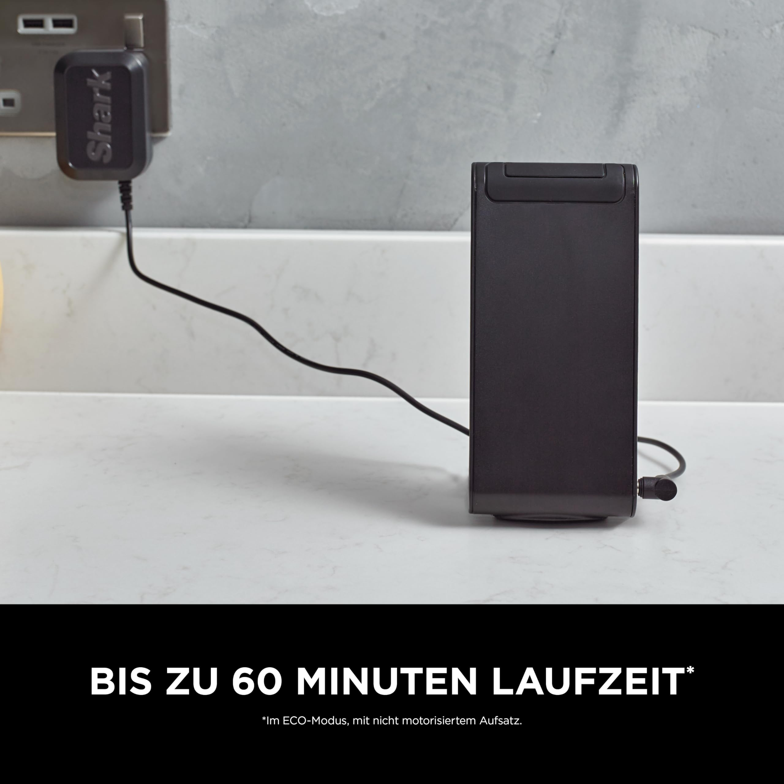 Ein schwarzes Shark-Gerät wird auf einer weißen Arbeitsplatte geladen und ist mit einem Kabel an eine Steckdose angeschlossen.