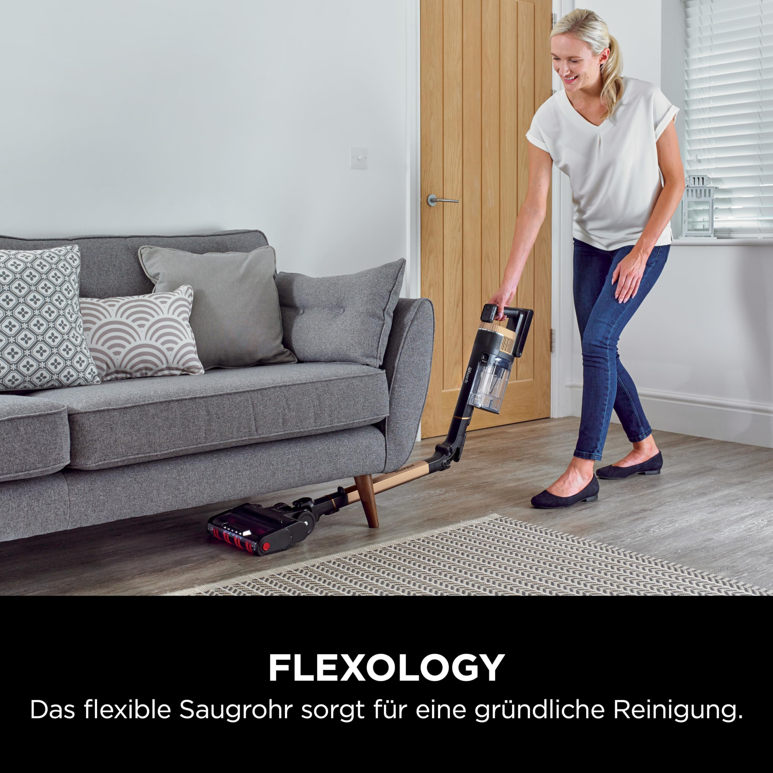 Eine Frau nutzt einen kabellosen Staubsauger, um unter dem Sofa zu reinigen.