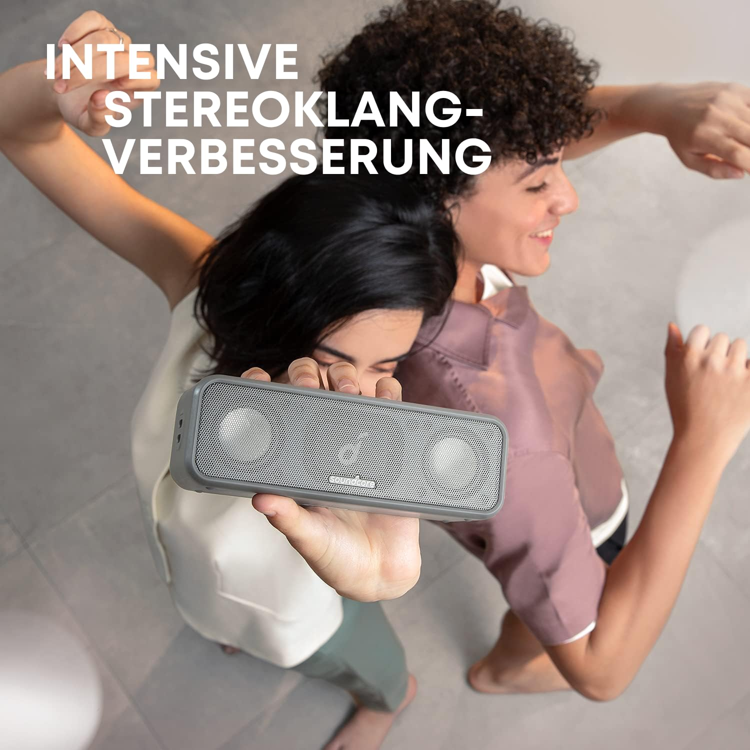 Due persone ballano felicemente tenendo in alto un altoparlante bluetooth Soundcore grigio.
