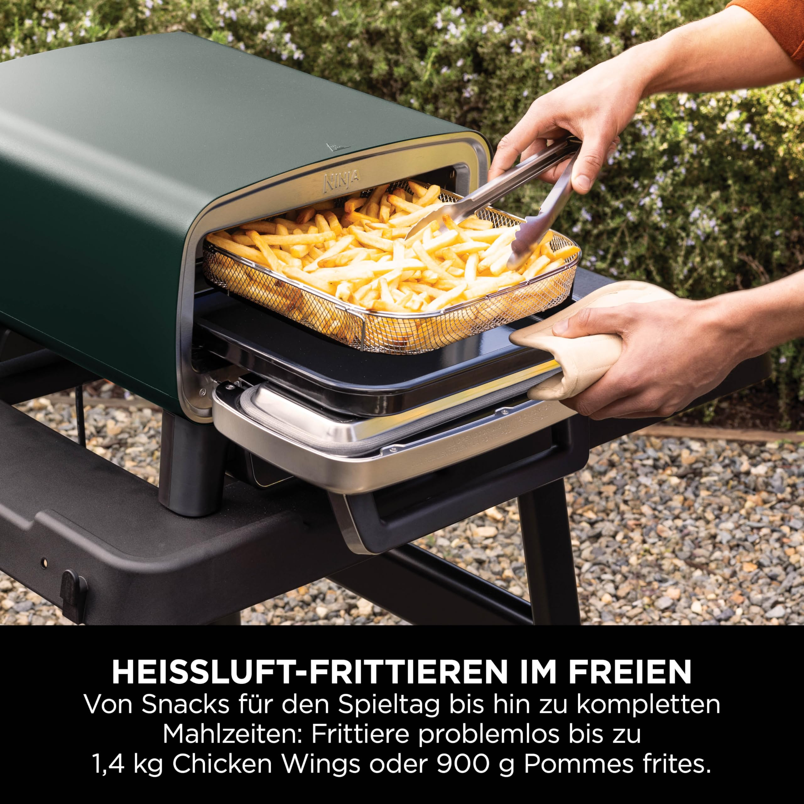 Une personne utilise des pinces pour retirer des frites d'une friteuse Ninja verte en extérieur.