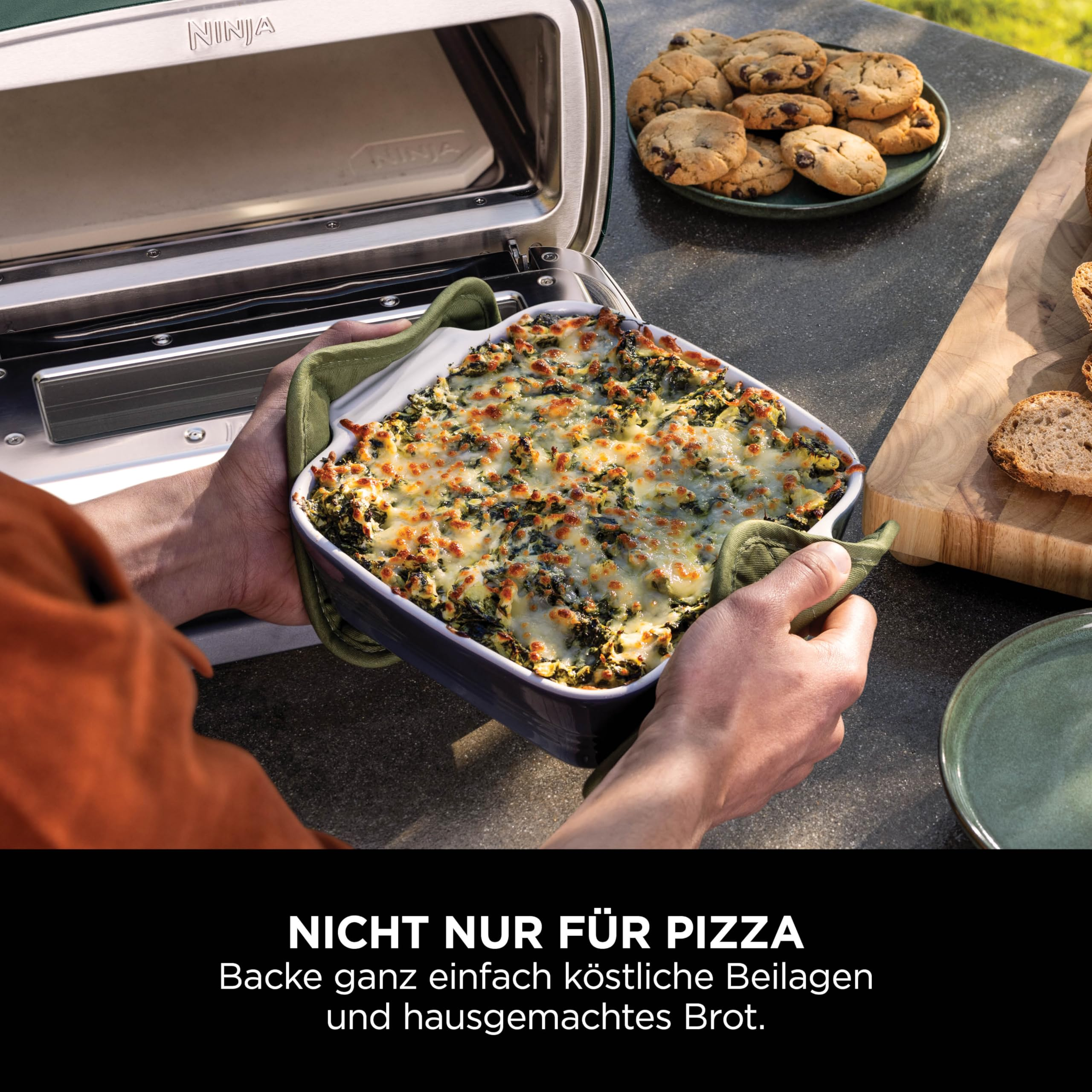 Personne tenant un plat à gratin cuit devant un four Ninja ouvert, avec des biscuits et du pain.
