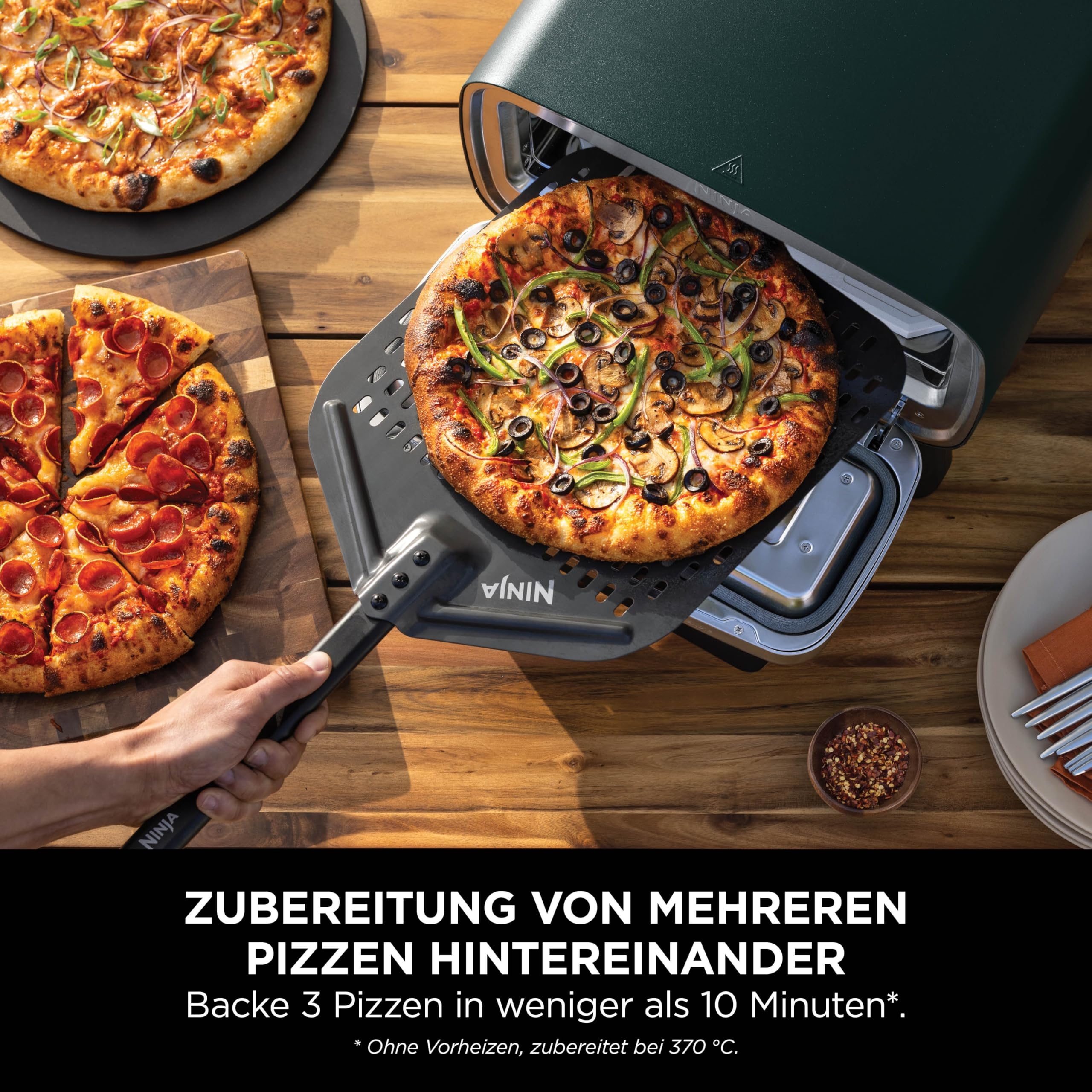 Une pizza est glissée dans un four Ninja vert avec une pelle, à côté d'une pizza au pepperoni.