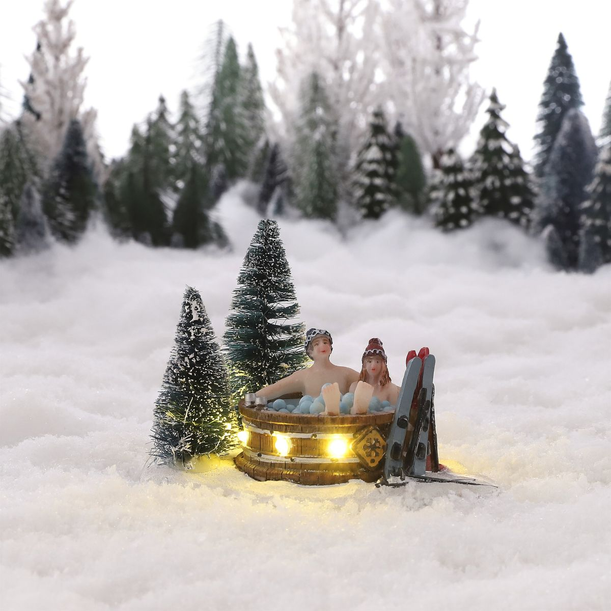 Couple miniature dans un bain à remous en bois éclairé dans la neige, avec skis.