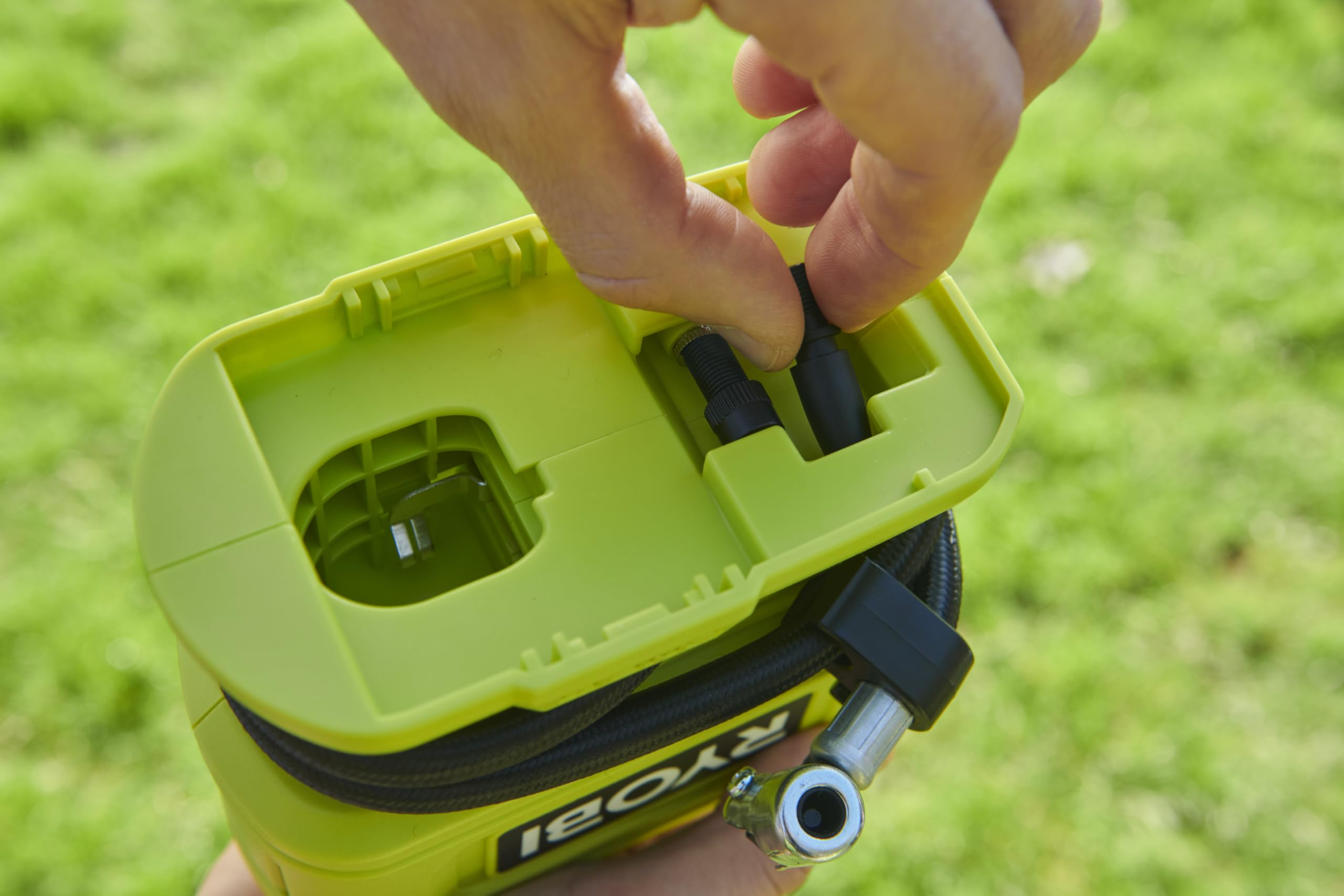Eine Hand nimmt Zubehörteile aus einer grünen Ryobi-Pumpe, Rasen im Hintergrund.