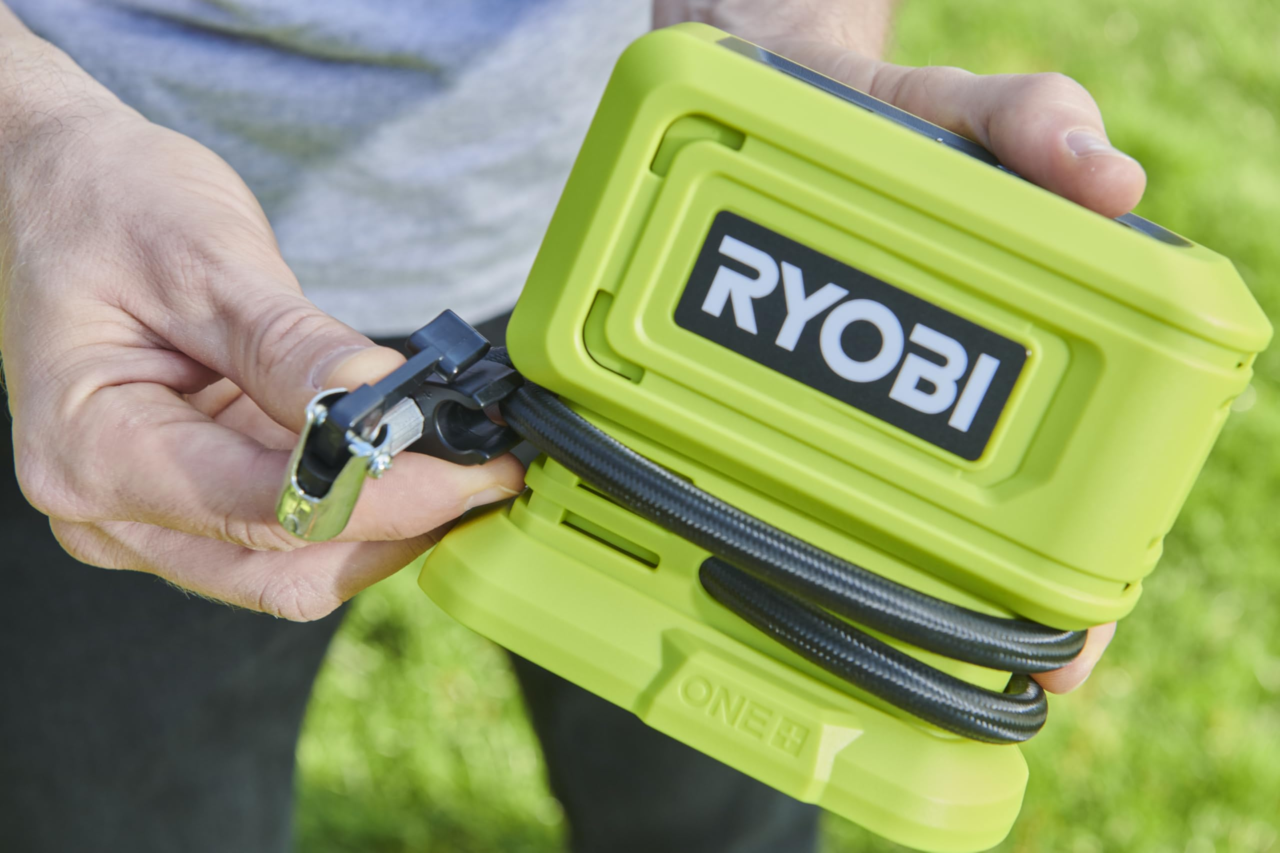 Eine Person hält eine grüne Ryobi-Luftpumpe mit aufgewickeltem Schlauch im Freien.