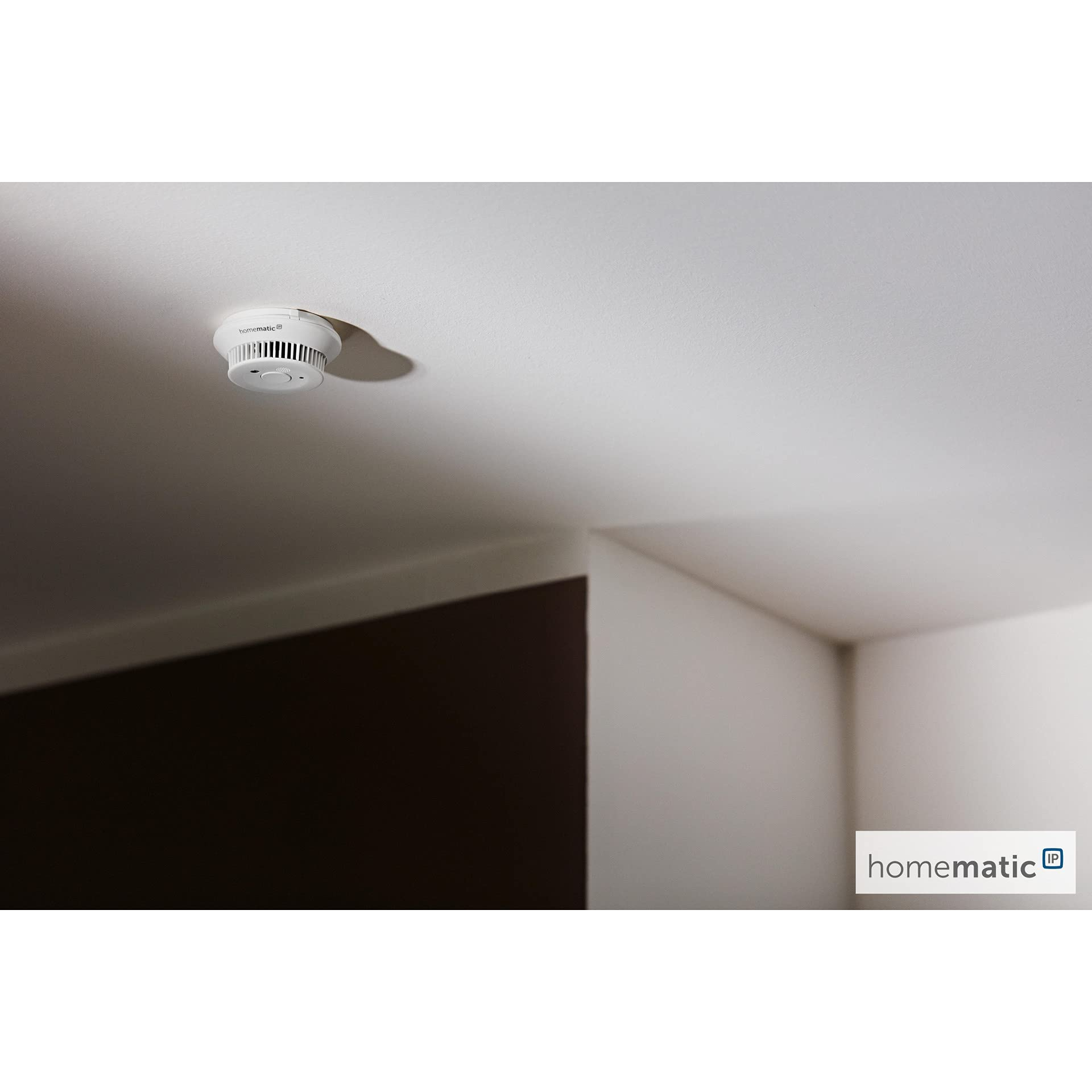 Un détecteur de fumée blanc fixé au plafond blanc d'une pièce moderne.