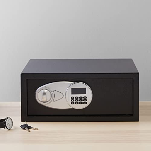 Ein schwarzer kleiner Tresor mit elektronischem Tastenfeld steht auf einem Holztisch, daneben liegen Uhren und Schlüssel.
