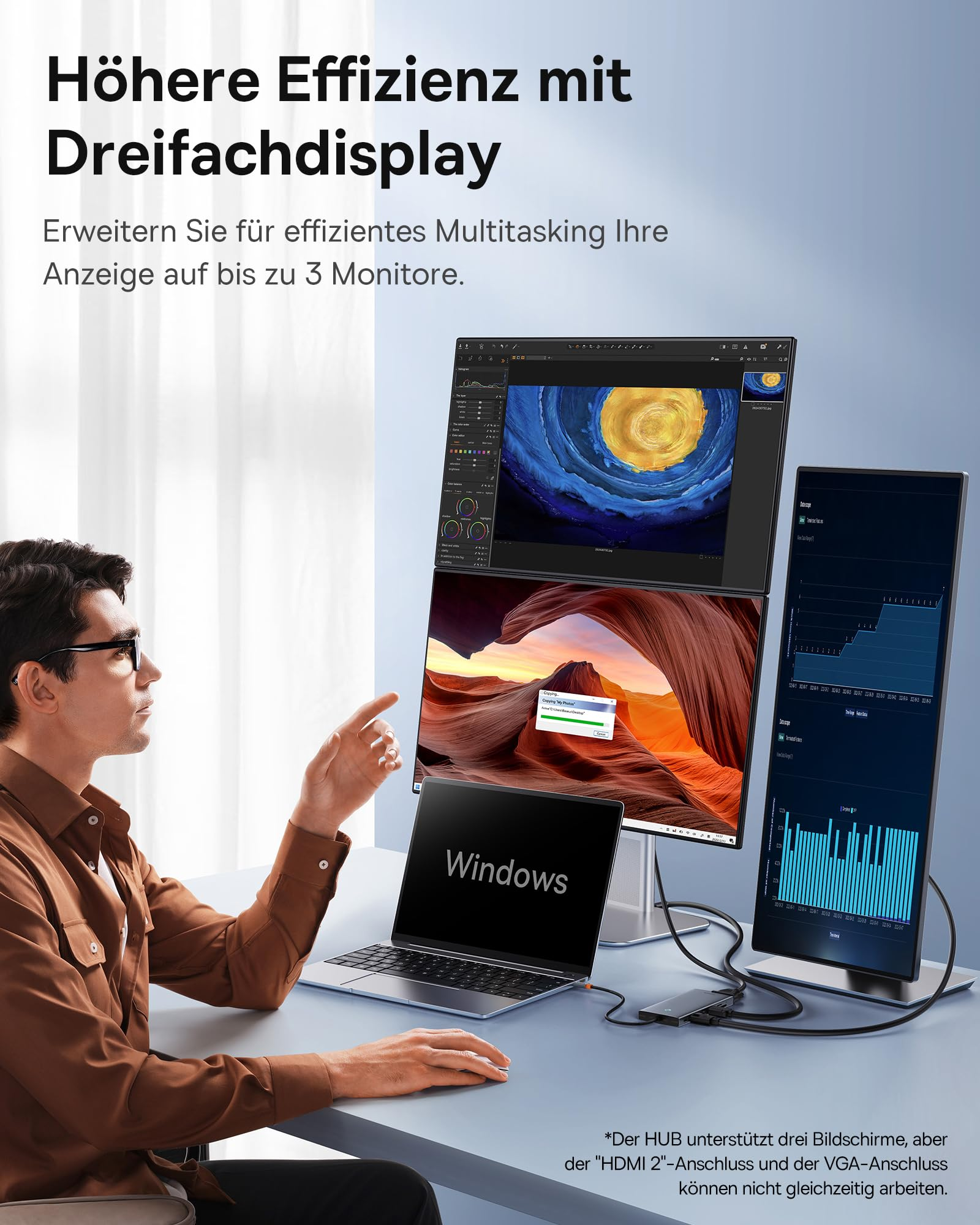 Un uomo lavora a una scrivania con un laptop e tre monitor collegati.