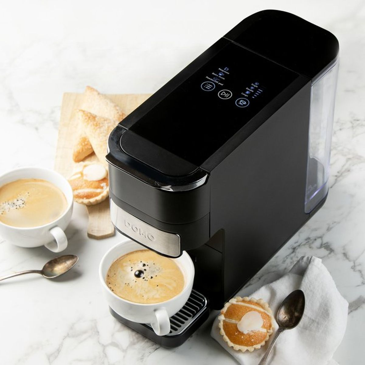 Schwarze Kaffeemaschine auf Marmorarbeitsplatte mit gefüllter Tasse, Gebäck und Löffel.