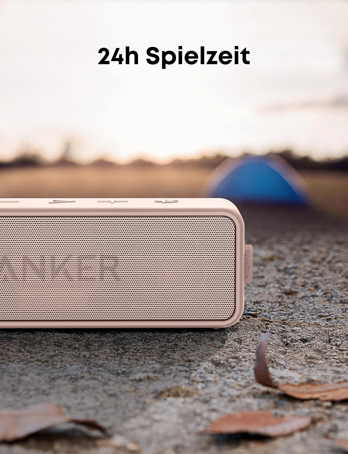 Haut-parleur Bluetooth rose au sol avec le texte 24h Spielzeit et une tente floue en arrière-plan.