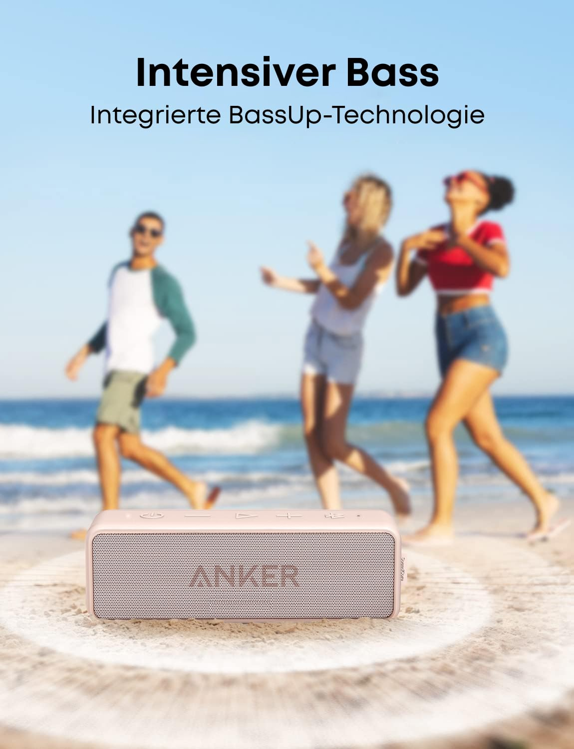Enceinte Bluetooth Anker rose au premier plan sur le sable, avec trois jeunes qui dansent sur une plage en arrière-plan.