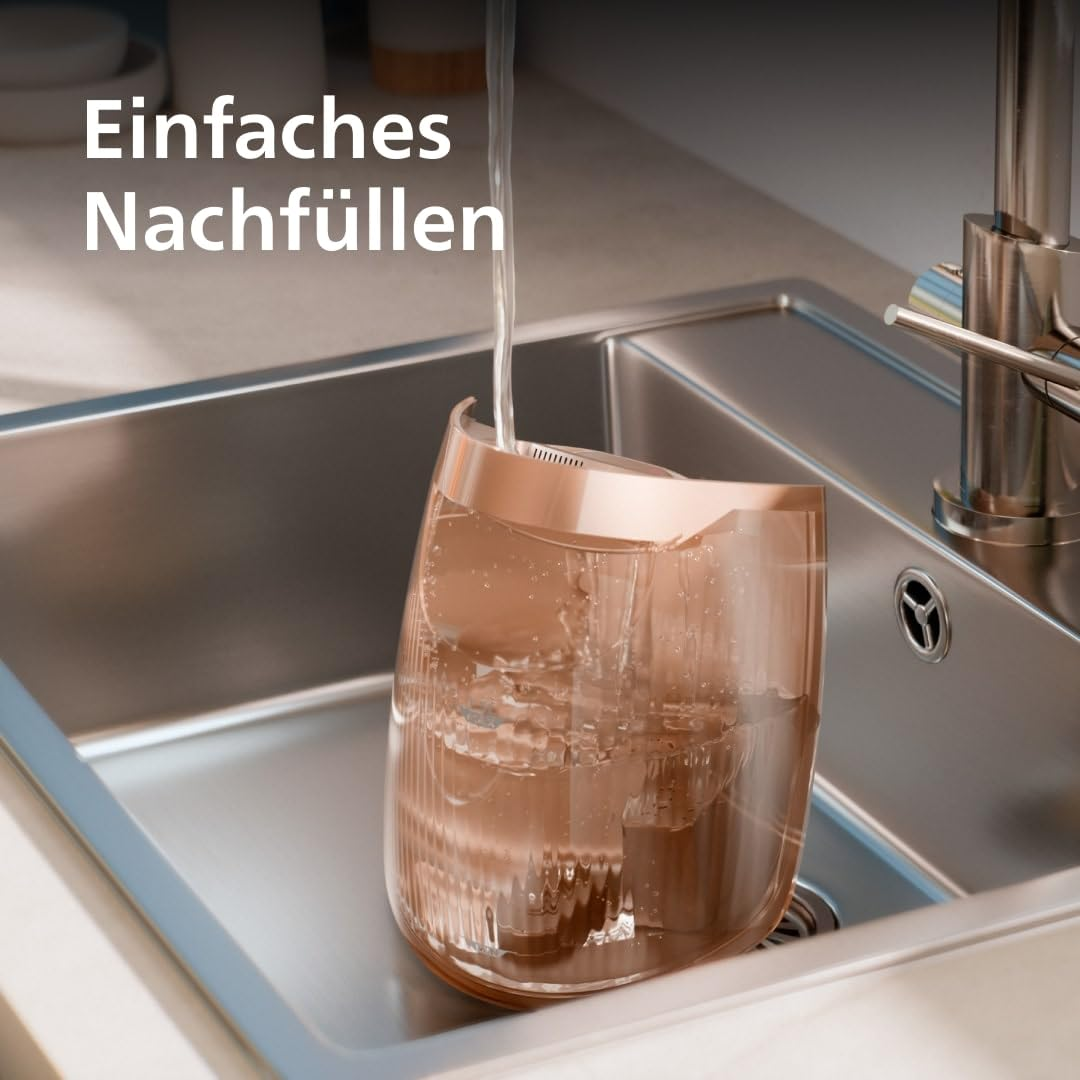 Wasser fließt aus einem Hahn in ein Roségoldenes Gerät in einer Edelstahlspüle.