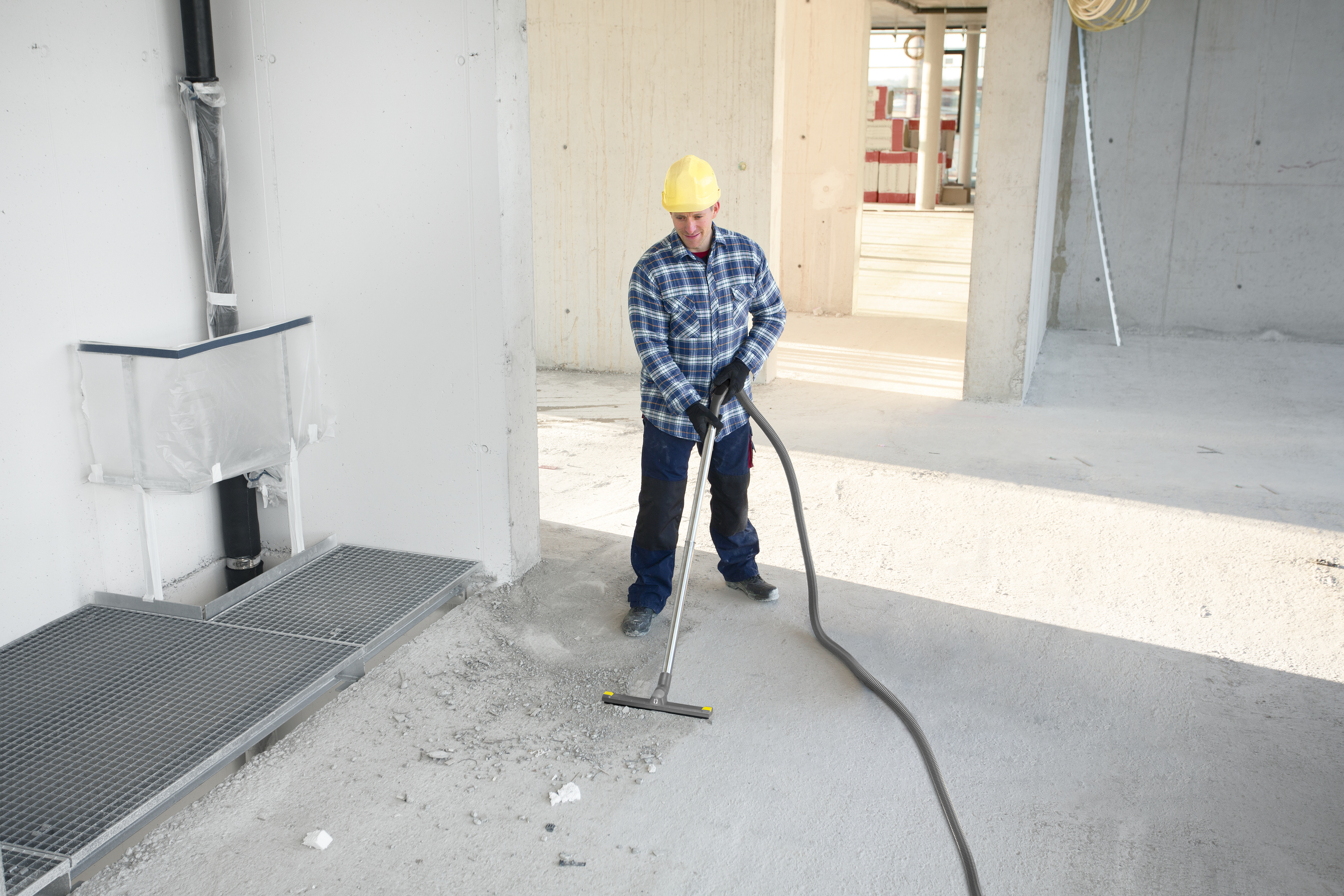 Ein Arbeiter mit gelbem Helm saugt den Betonboden auf einer Baustelle ab.
