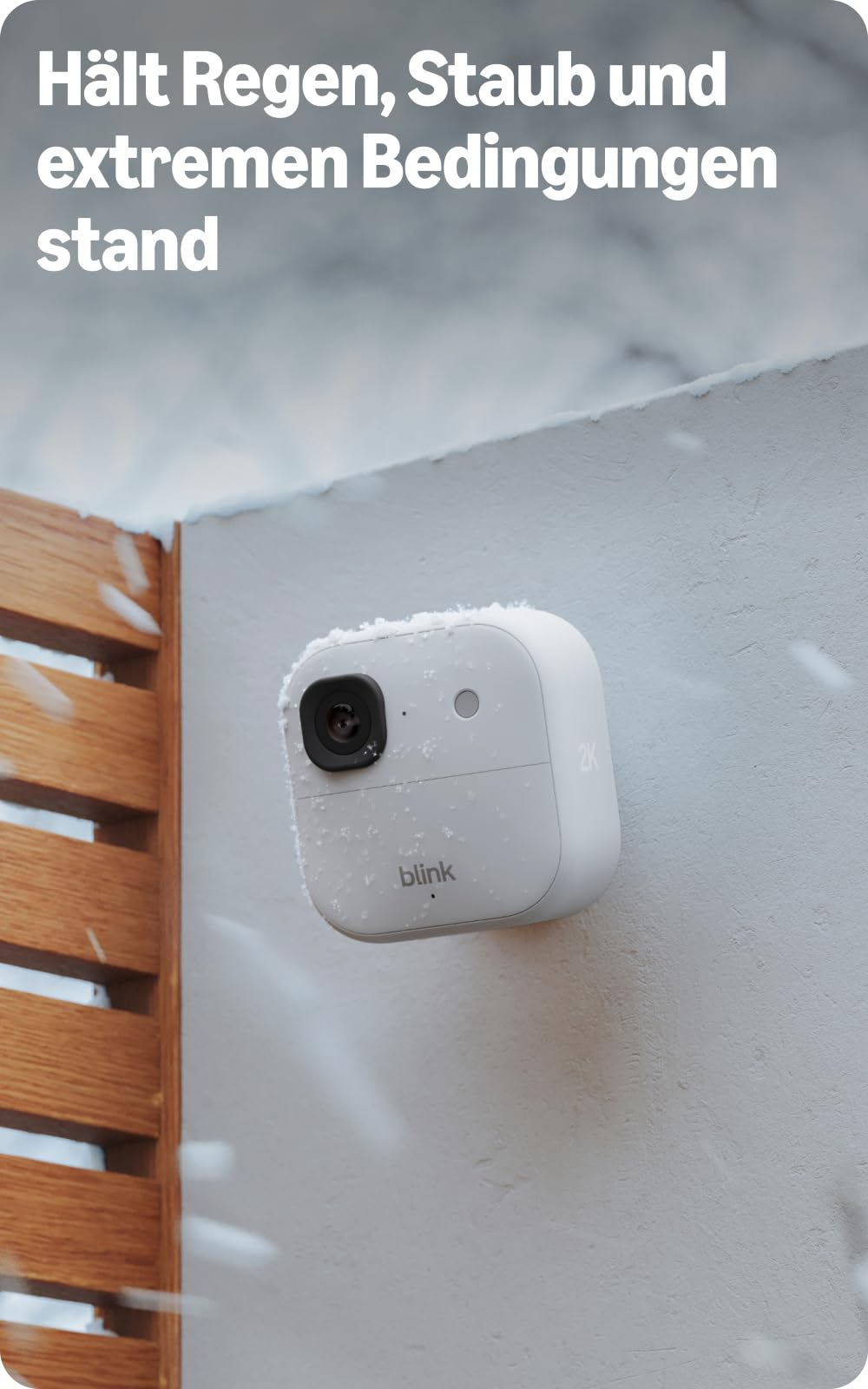 Una telecamera di sicurezza bianca Blink montata su un muro innevato durante una nevicata.