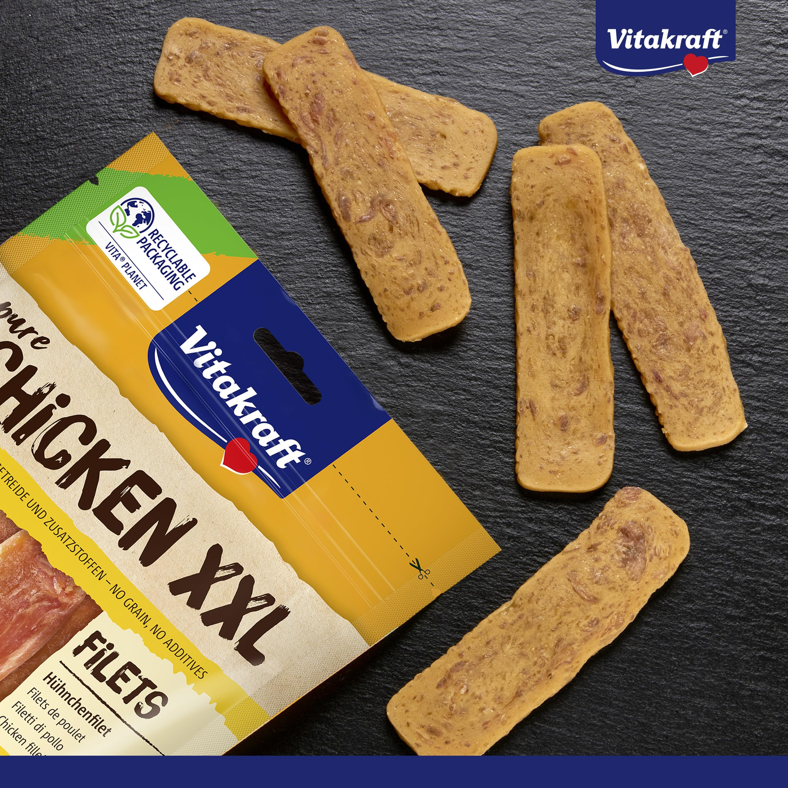 Vitakraft Chicken XXL Leckerlibeutel mit verstreuten Fleischsnackstreifen auf dunkler Schieferoberfläche.
