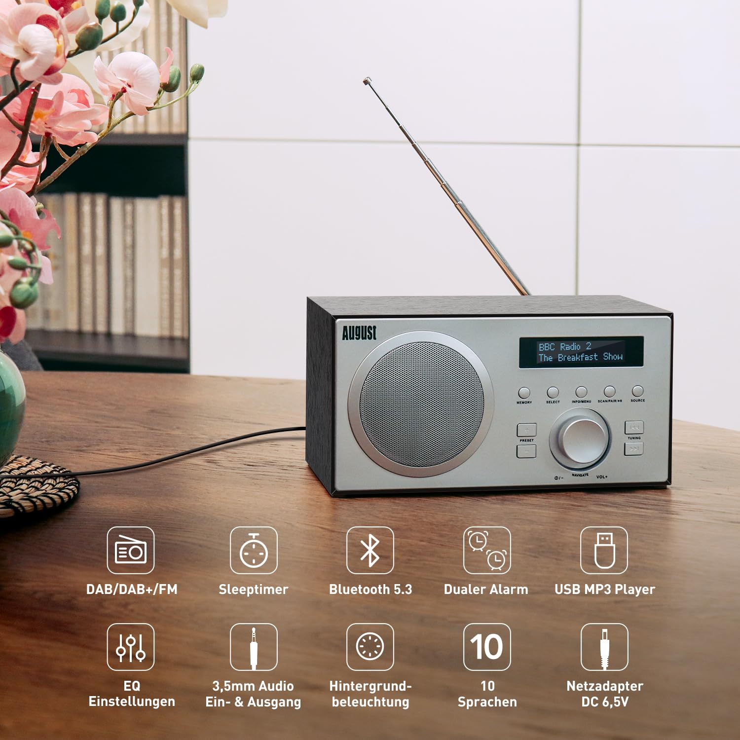 Una radio digitale August argento e nera su un tavolo di legno, con icone di funzioni.
