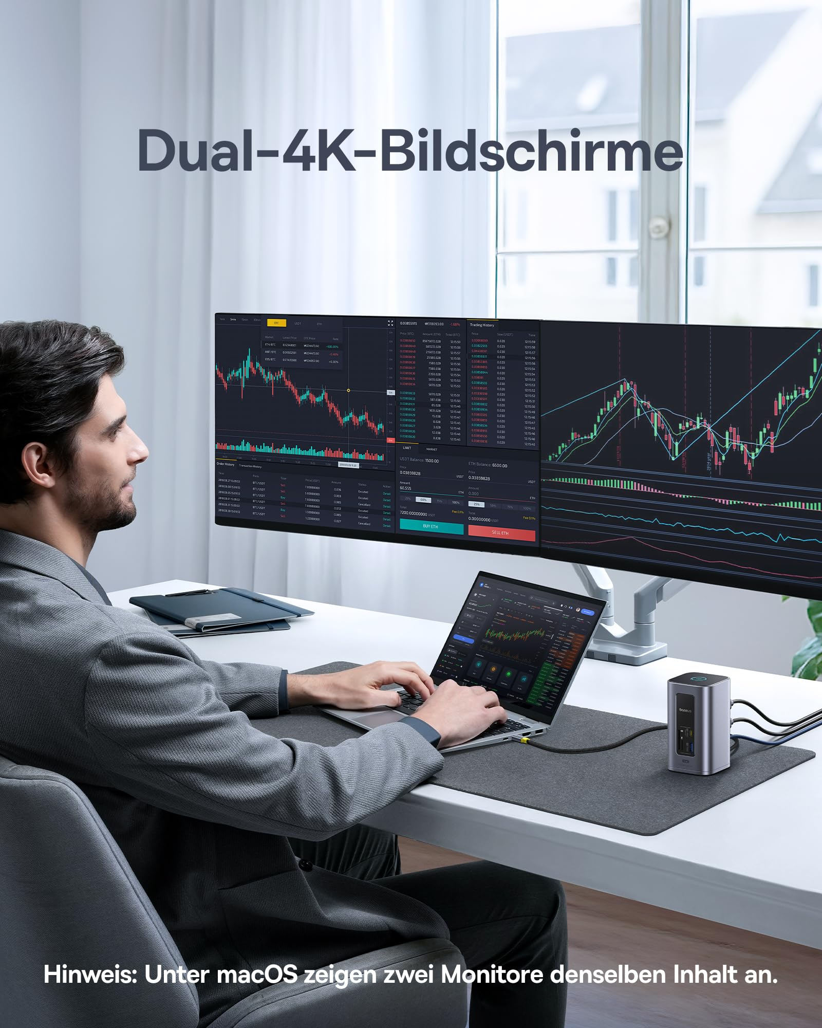 Ein Mann sitzt an einem Schreibtisch und arbeitet an einem Laptop vor einem großen Dual-Monitor mit Börsendaten.