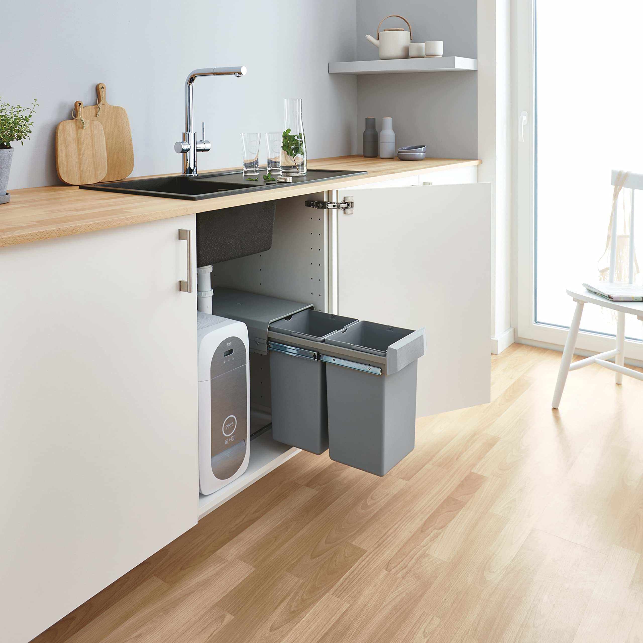 Küchenzeile mit geöffnetem Schrank, grauen Auszugseimern und Wasserträger unter einem schwarzen Becken.