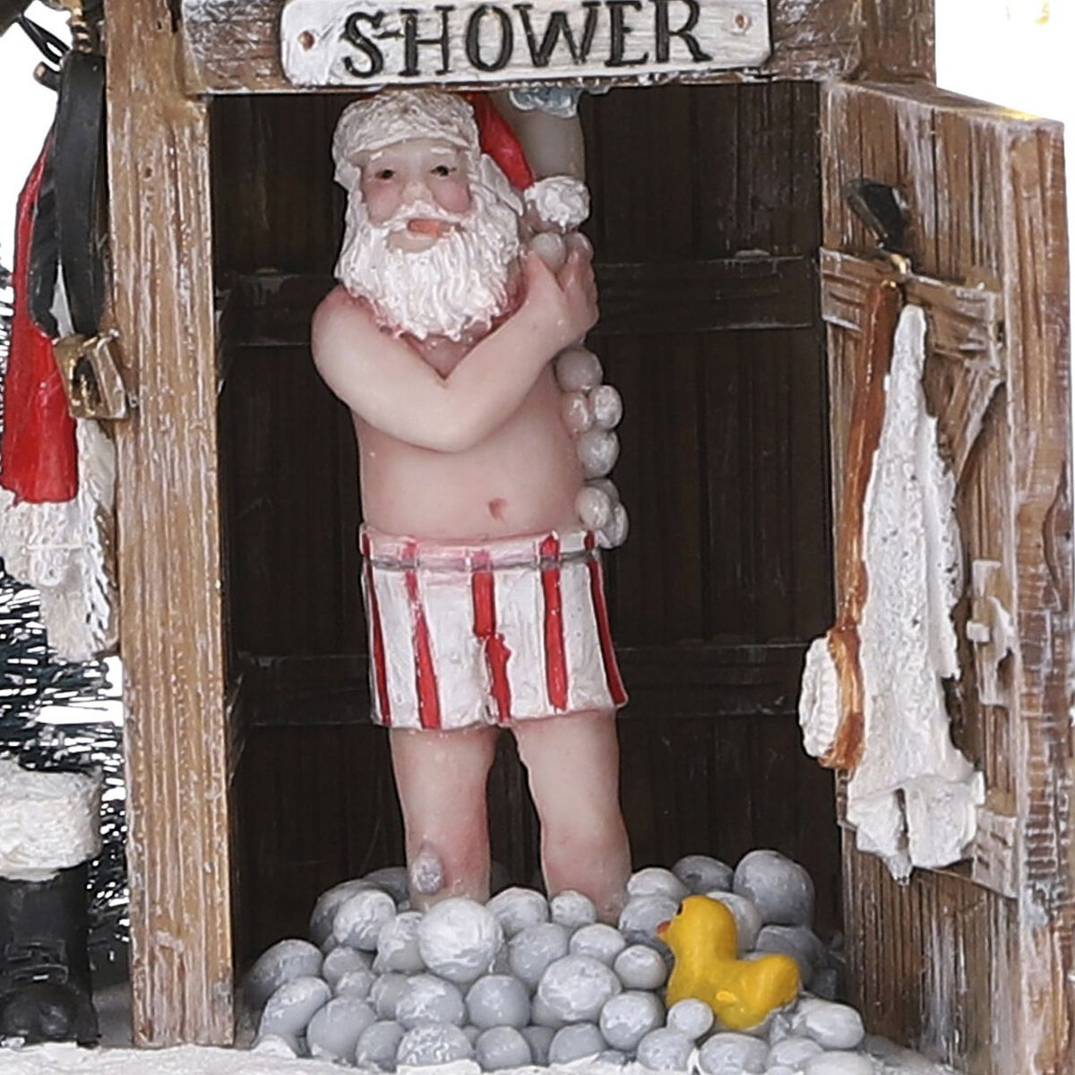 A Santa Claus figurine in striped swim shorts showering in a wooden shower with many soap bubbles and a yellow duck.