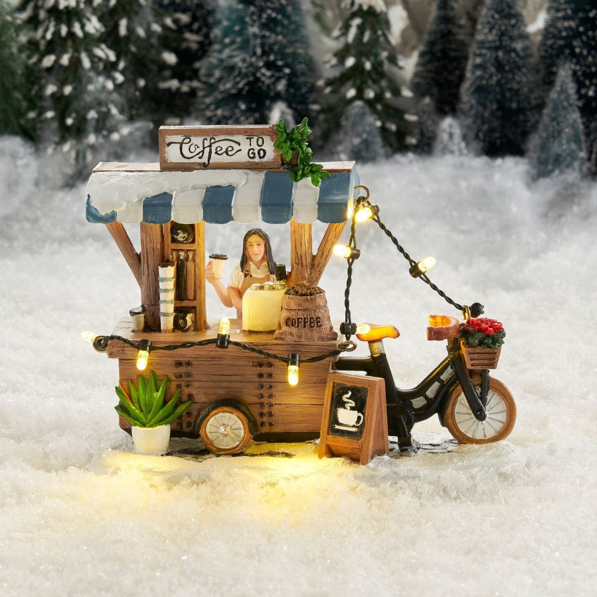 Een miniatuur koffiekar met lichtjes in een besneeuwd landschap met fiets.