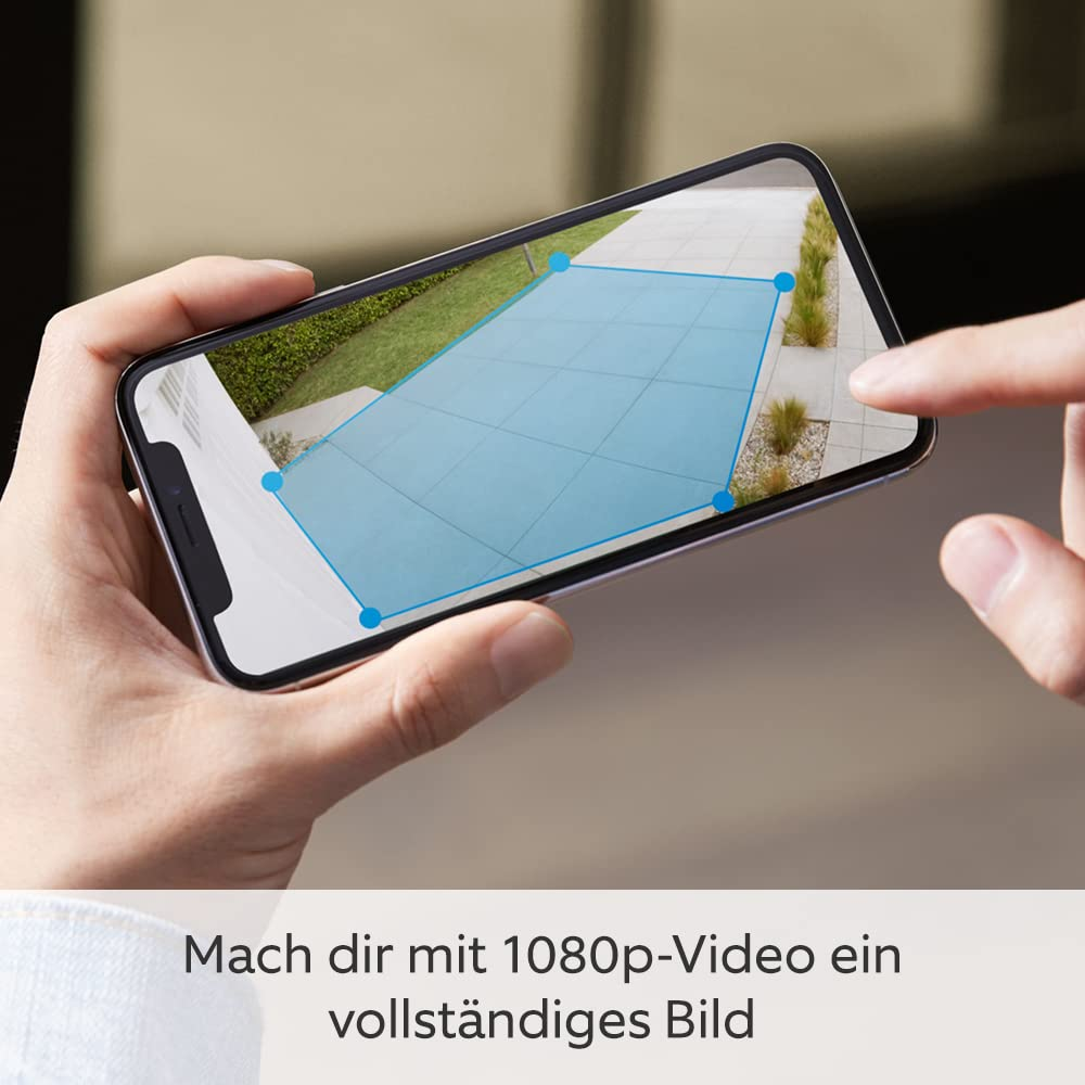 Una persona tiene in mano uno smartphone con la vista di una telecamera esterna e una zona blu.