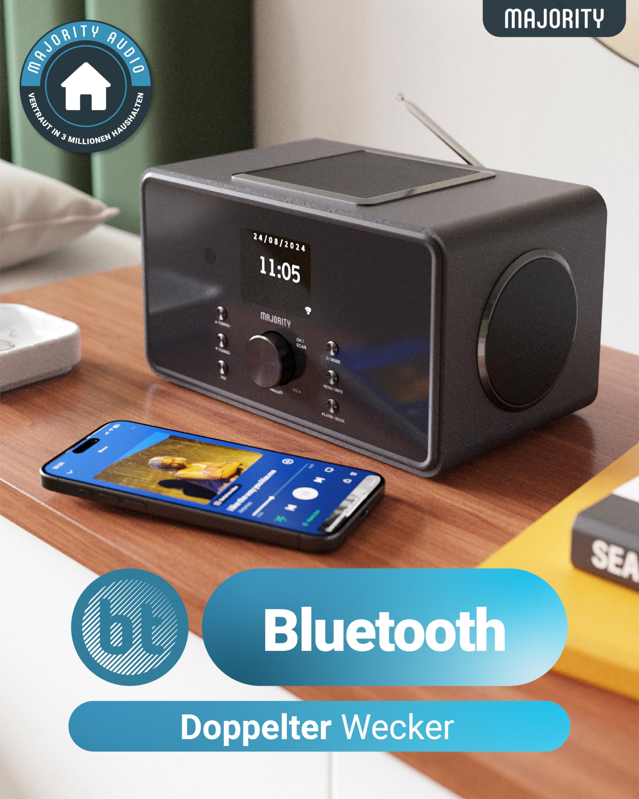 Ein graues Digitalradio und ein Smartphone mit Musik-App liegen auf einem Holztisch.