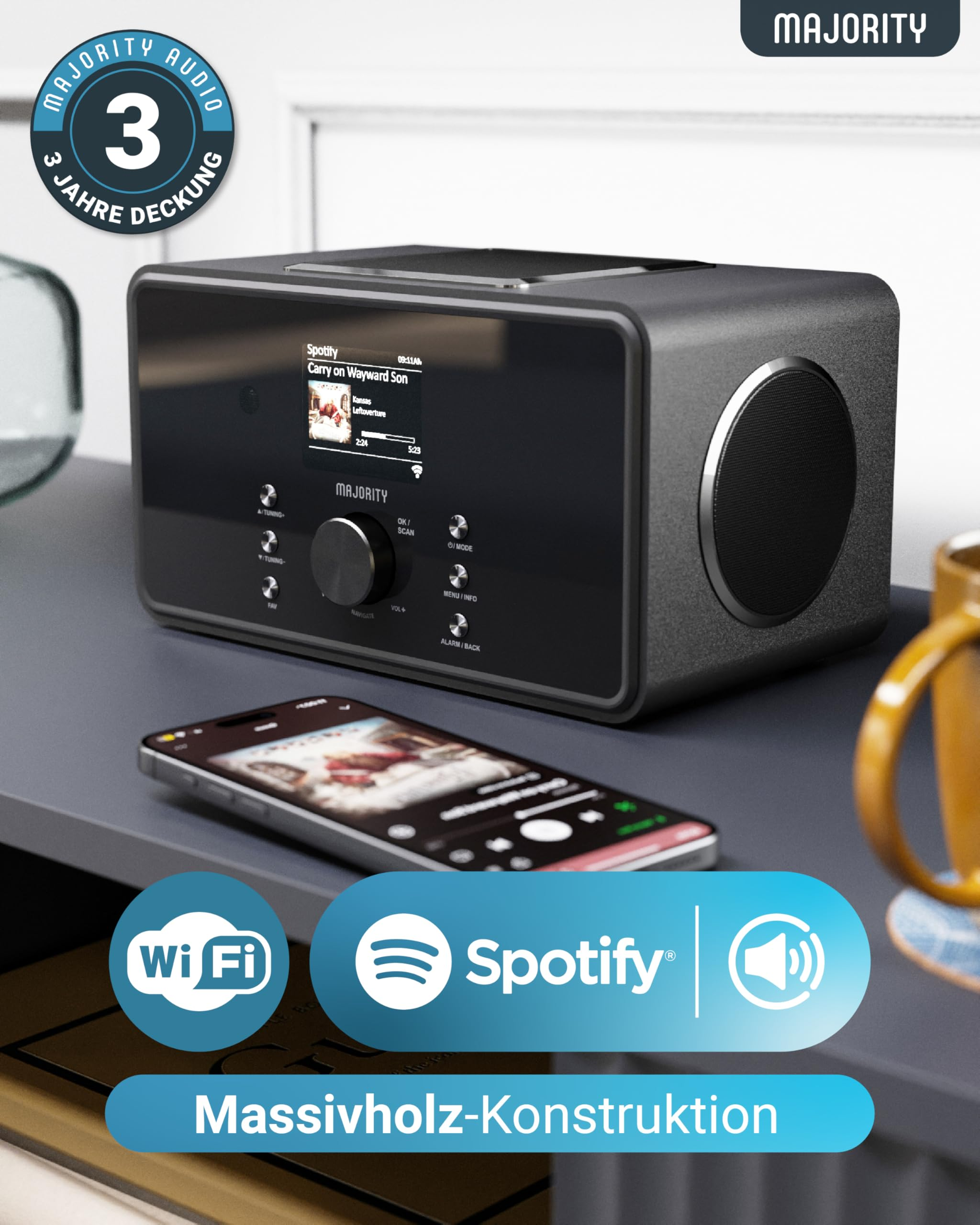 Ein dunkles Mehrzweckradio mit Spotify-App auf dem Display, einem Smartphone davor und Werbeelementen.