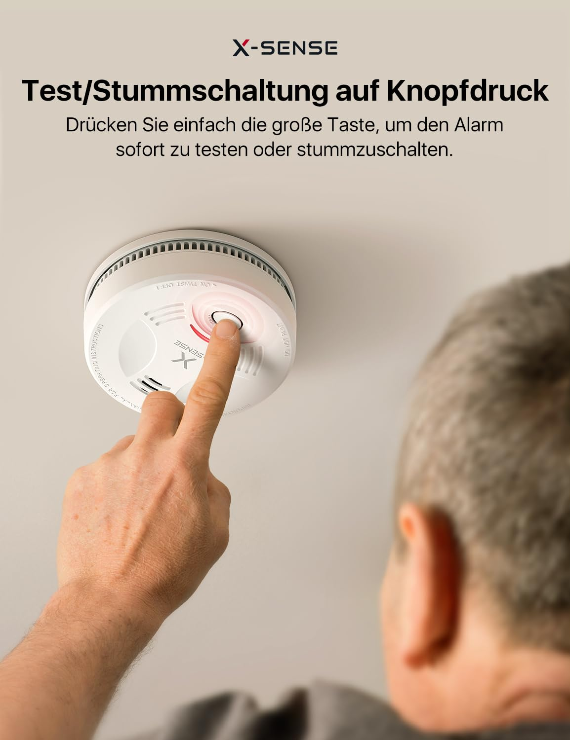 Un homme appuie sur le bouton de test d'un détecteur de fumée X-Sense blanc au plafond.