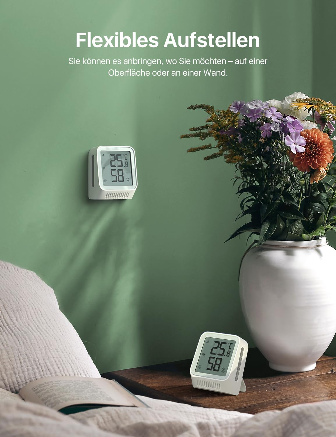 Un thermomètre numérique blanc sur un mur vert et un autre sur une table de chevet en bois près d'un vase.