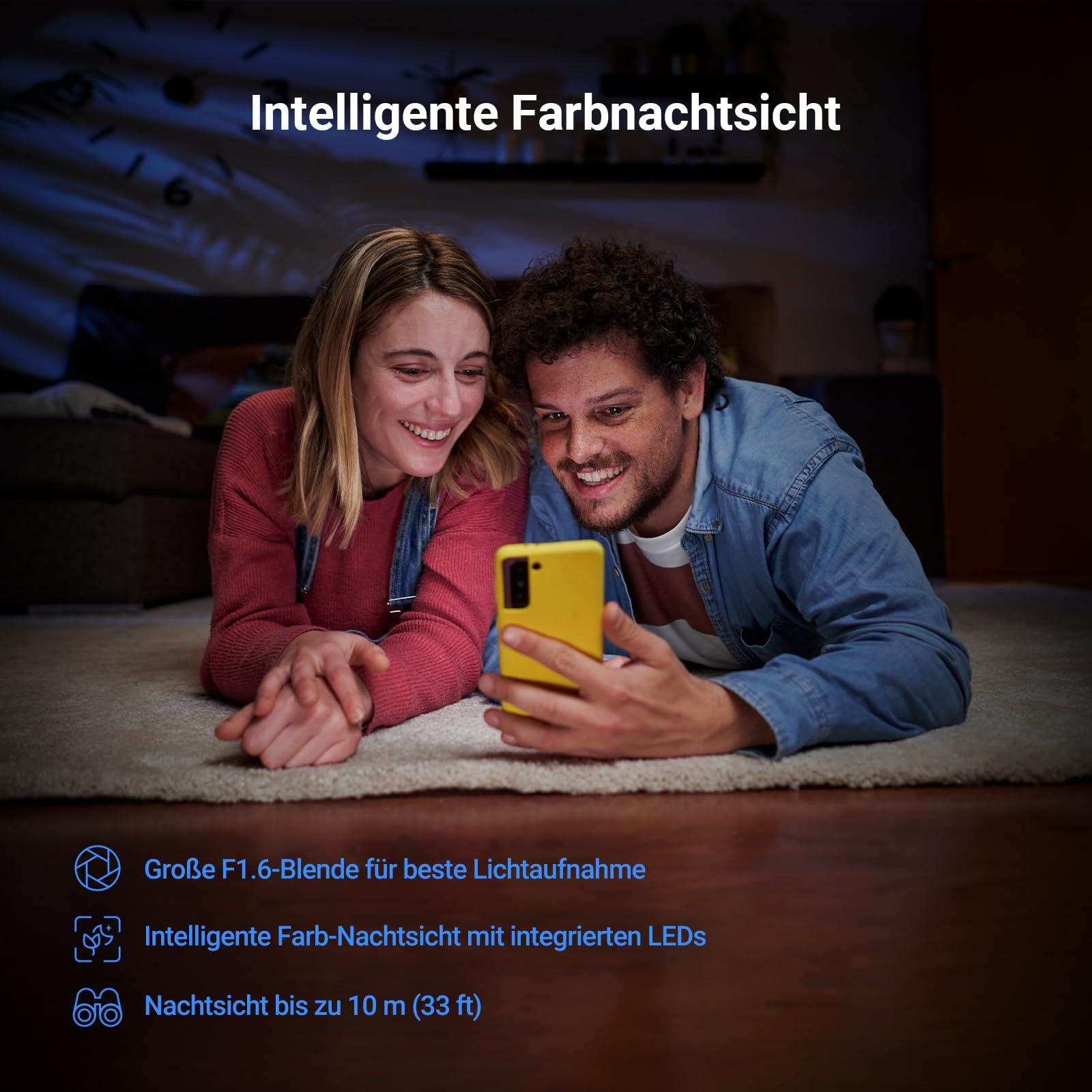 Una coppia sorridente sdraiata su un tappeto guarda uno smartphone giallo al buio.