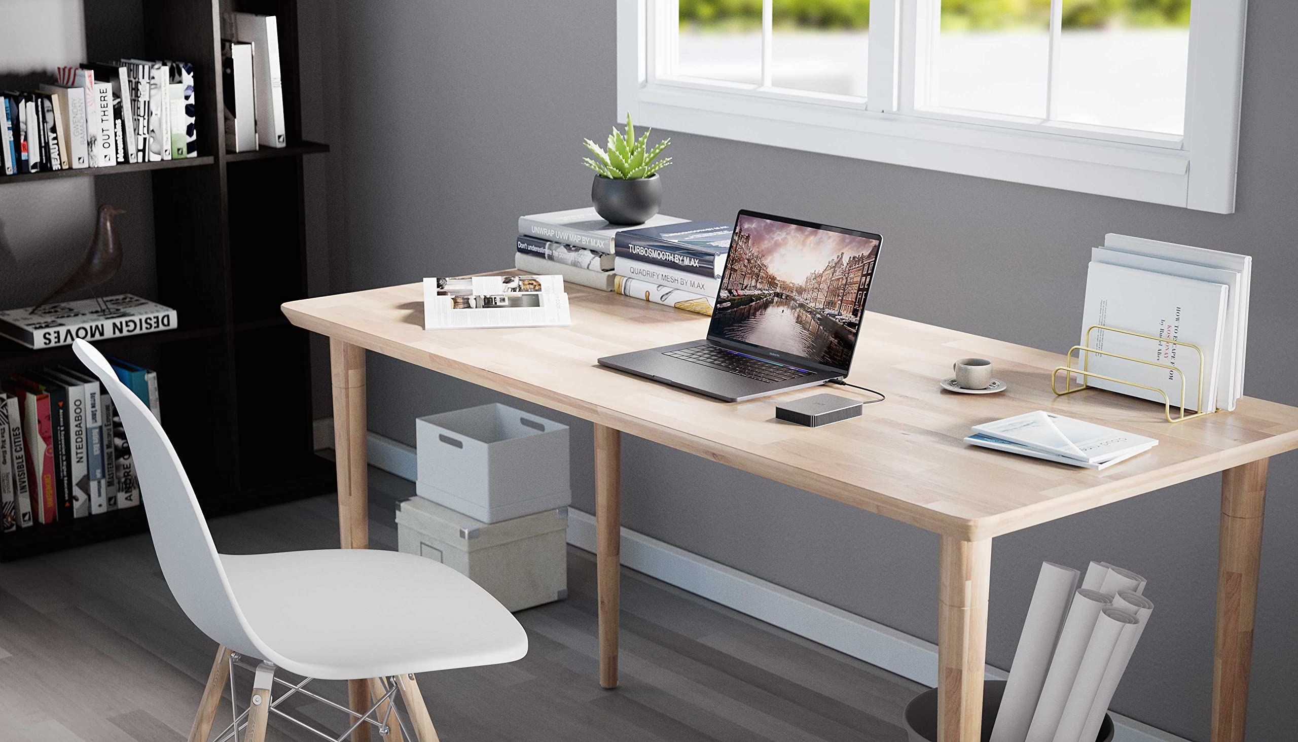 Una scrivania in legno con laptop, libri, pianta e tazza in un ufficio moderno.