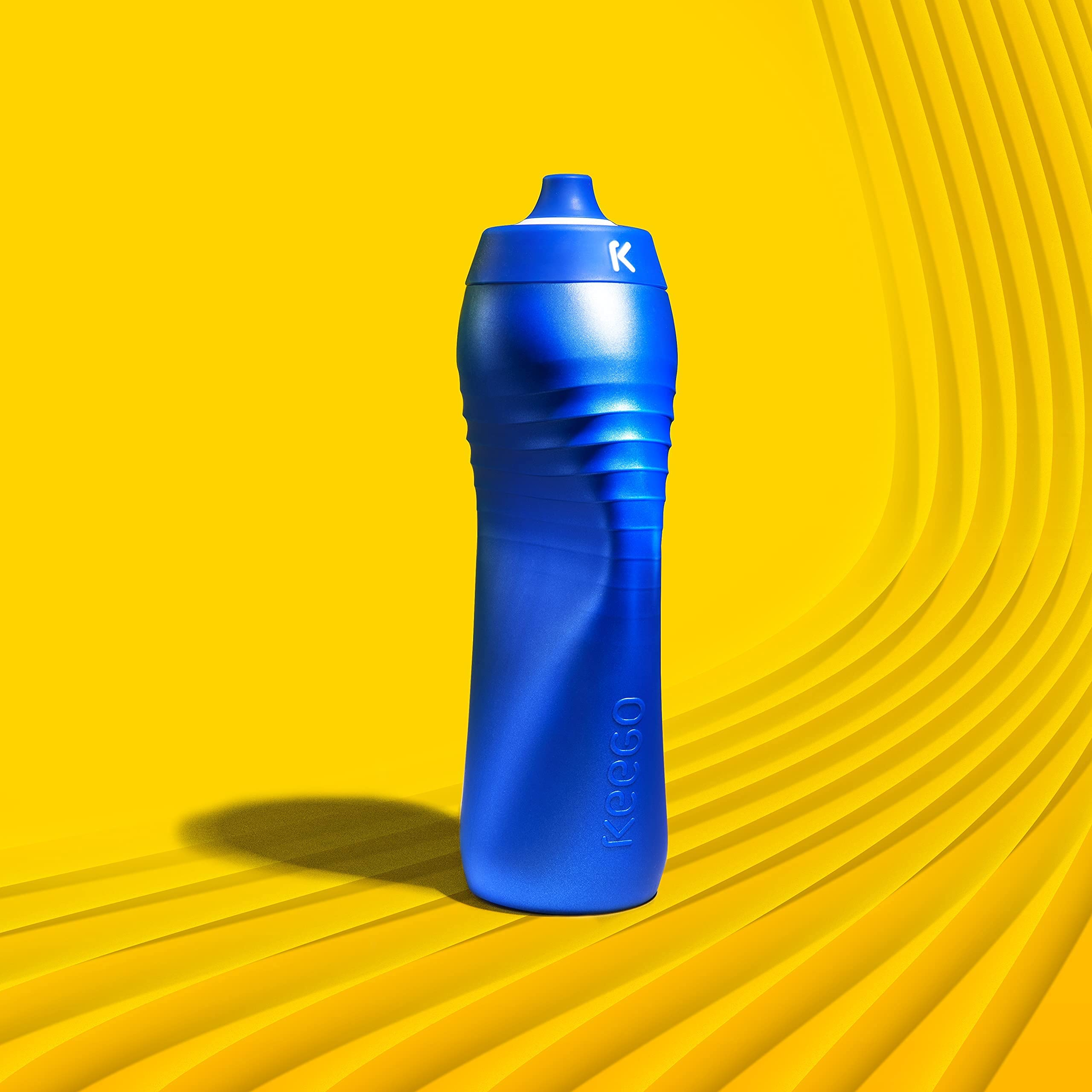 Eine blaue Keego Trinkflasche steht auf einer gelben, strukturierten Oberfläche vor einem gelben Hintergrund.