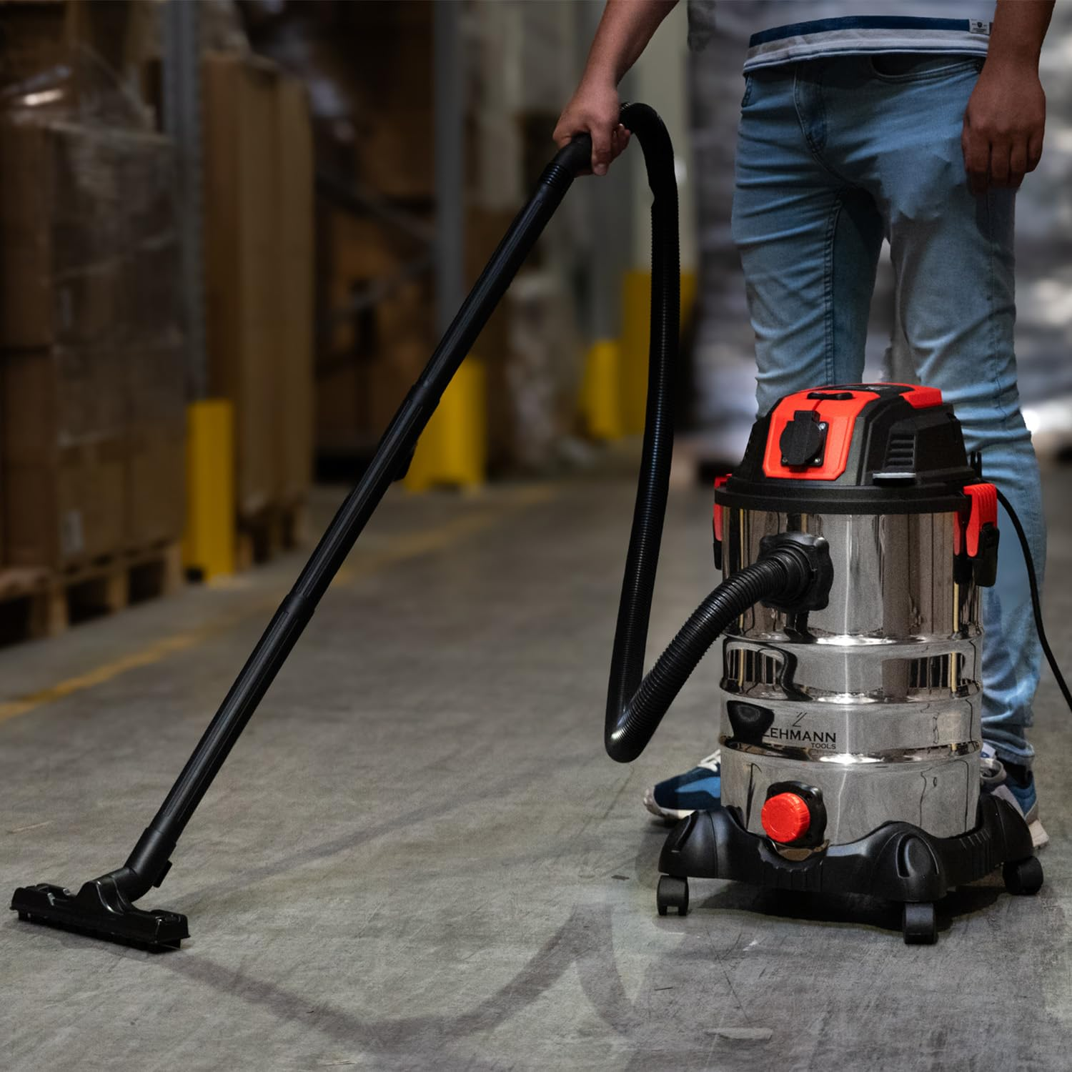 Una persona usa un grande aspirapolvere industriale argentato con tubo nero in un magazzino.