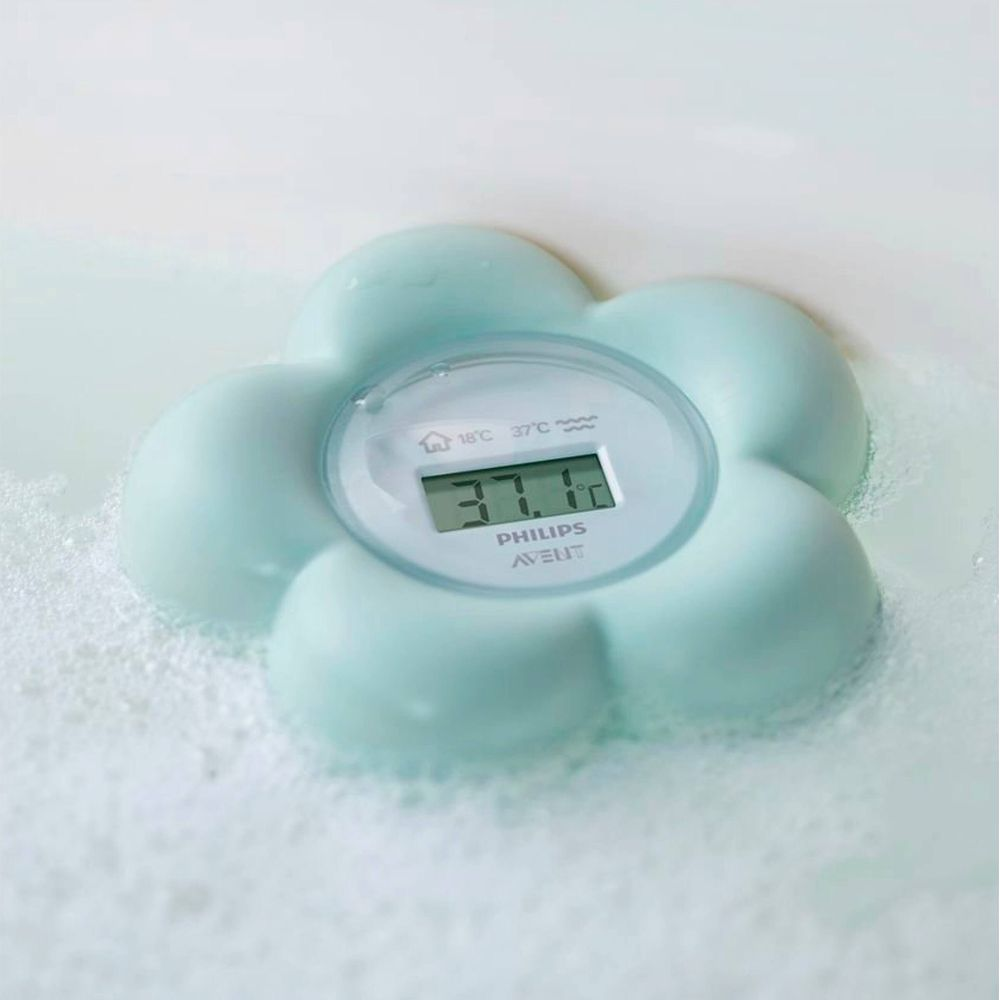 Ein mintgrünes, blumenförmiges Philips Avent Badethermometer schwimmt in Schaumwasser.