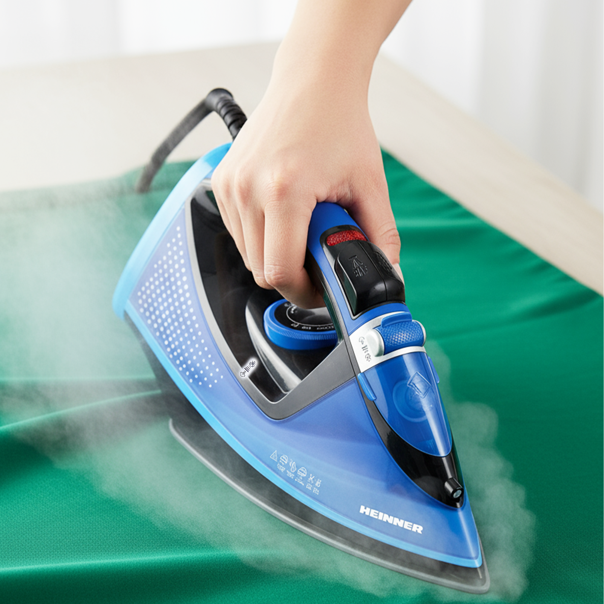 A hand irons green clothing with a blue steam iron.