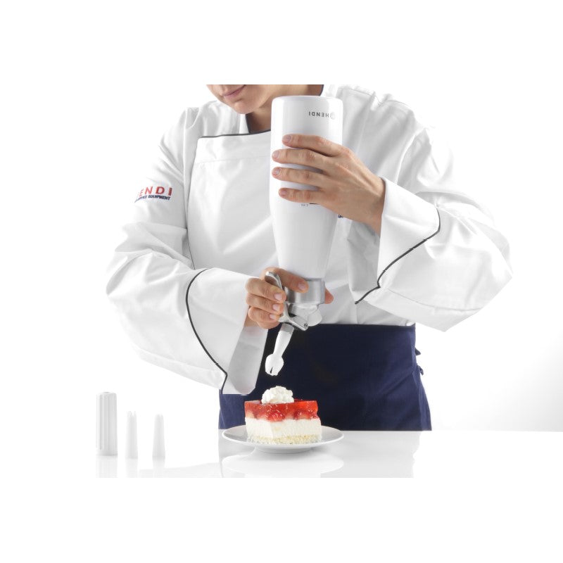 Koch in weißer Uniform dekoriert einen Erdbeerkuchen auf einem Teller mit einer Sahnespritze.
