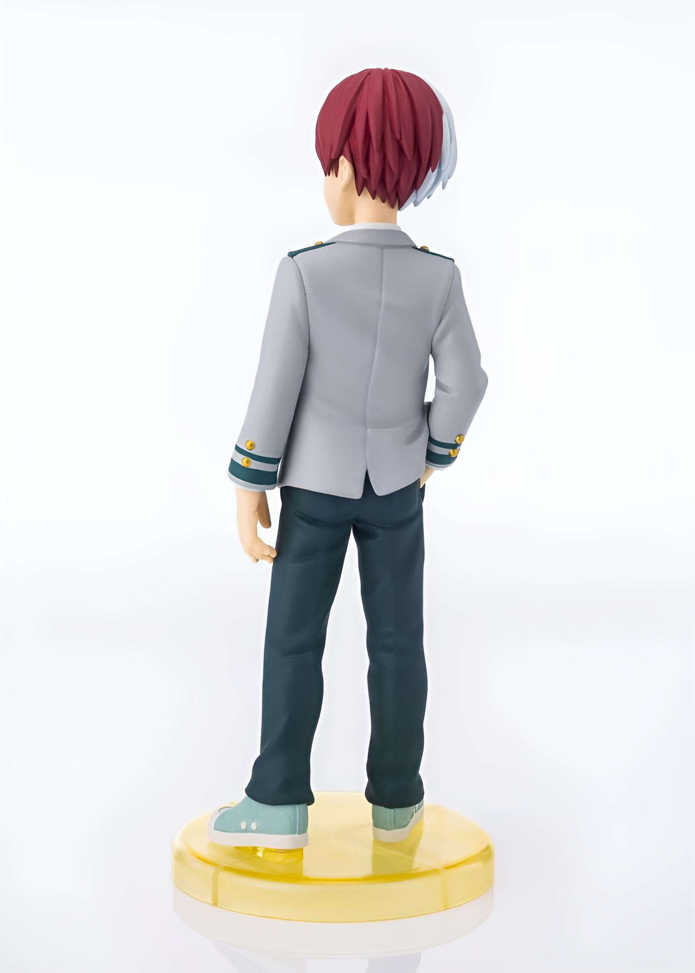 Figura de anime desde atrás con pelo rojo y blanco, chaqueta gris, pantalones oscuros sobre base amarilla.