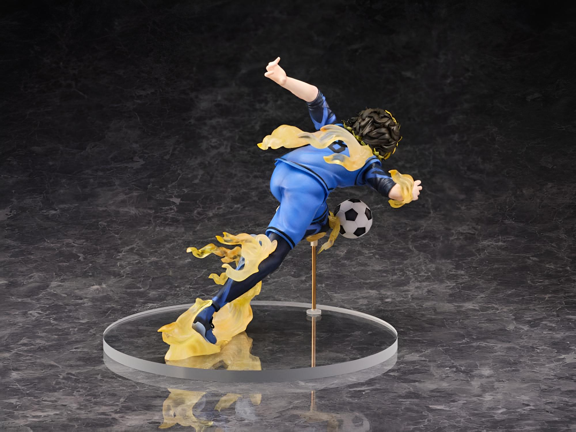 Una figura de futbolista con camiseta azul chuta un balón con efectos de llamas amarillas sobre una base redonda.