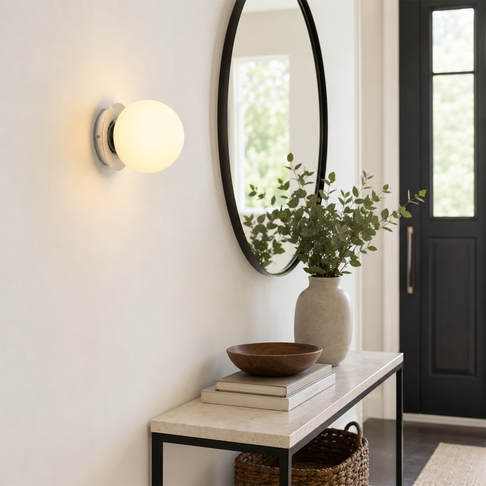 Un aplique de pared con esfera blanca brilla sobre una mesa consola con espejo y florero en un pasillo.