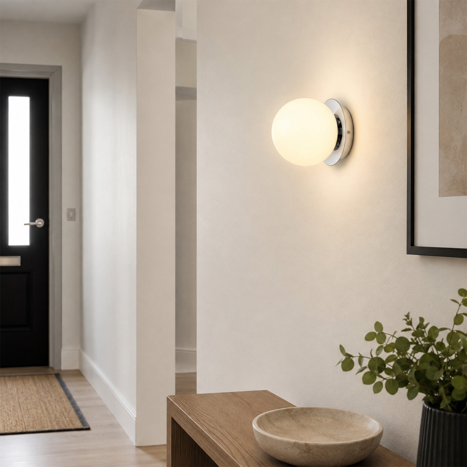Un aplique de pared con esfera blanca ilumina un pasillo moderno con puerta negra y muebles de madera.