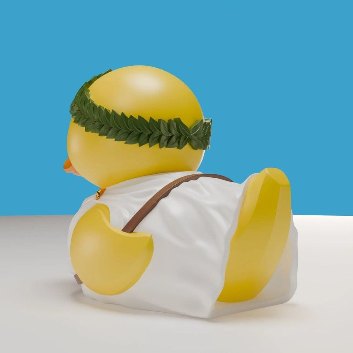Eine gelbe Ente mit Lorbeerkranz und Toga sitzt auf einem weißen Tisch vor blauem Hintergrund.