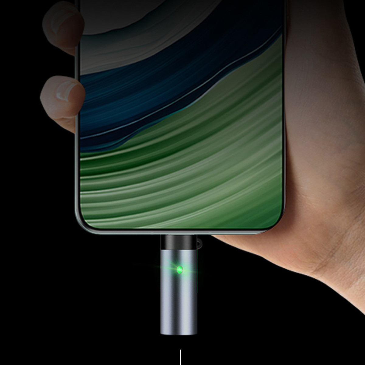 Ein Smartphone wird in der Hand gehalten, während ein kleiner silberner Magnetadapter mit grünem Licht unten angeschlossen ist.