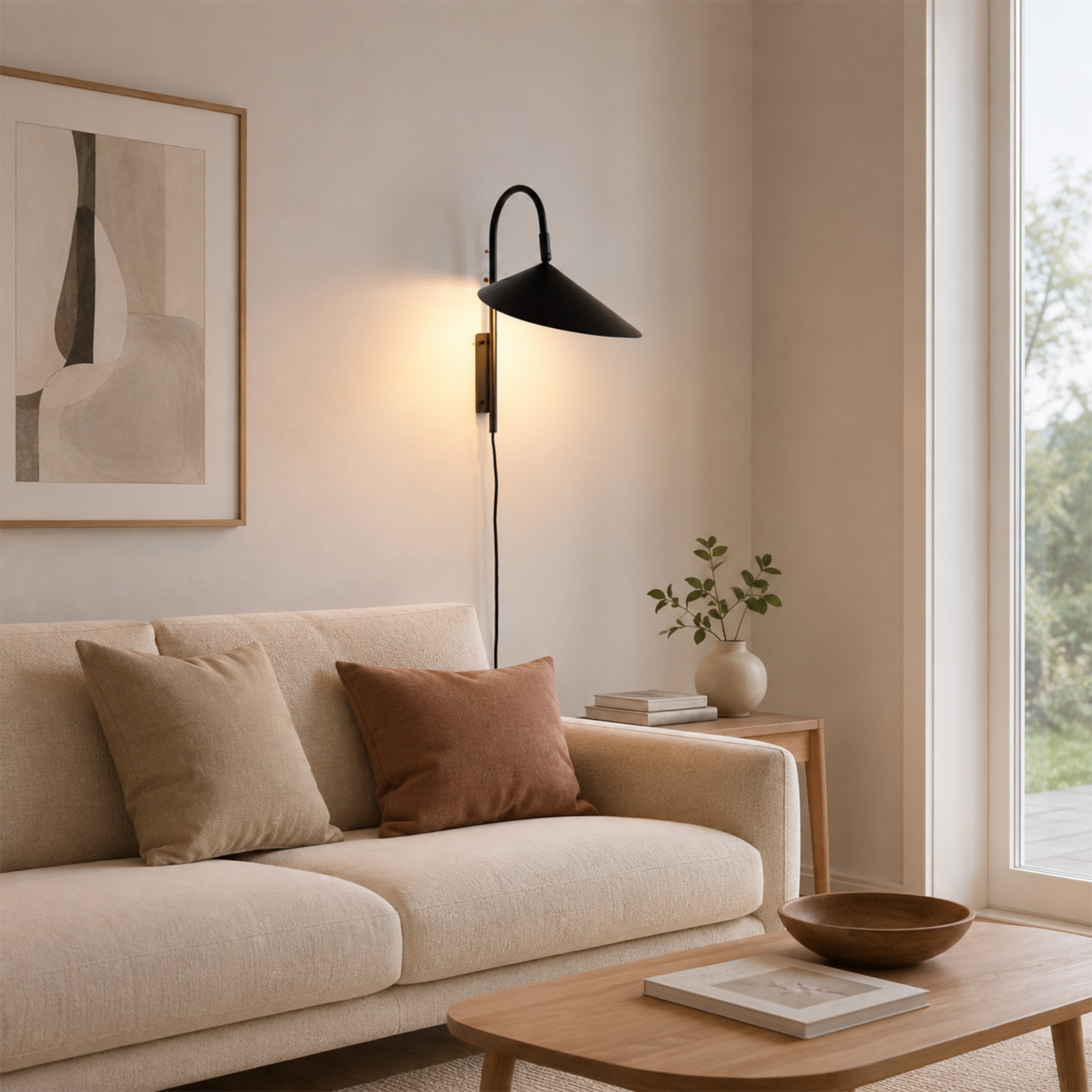 Sala de estar acogedora con sofá beige, cojines, aplique de pared, cuadro y mesa de centro con libro y cuenco.