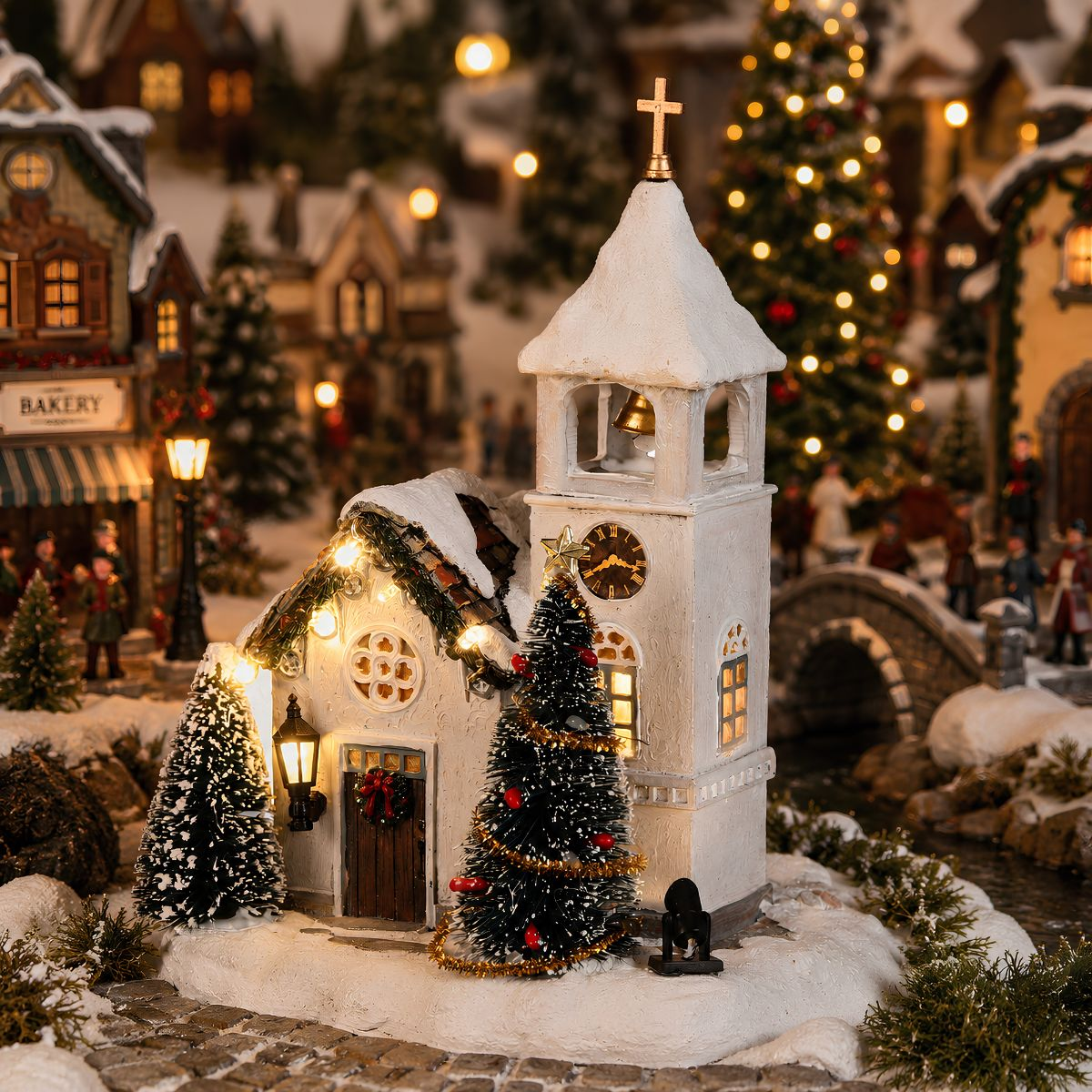 Een besneeuwd miniatuurdorp met een verlichte kerk en versierde kerstbomen.