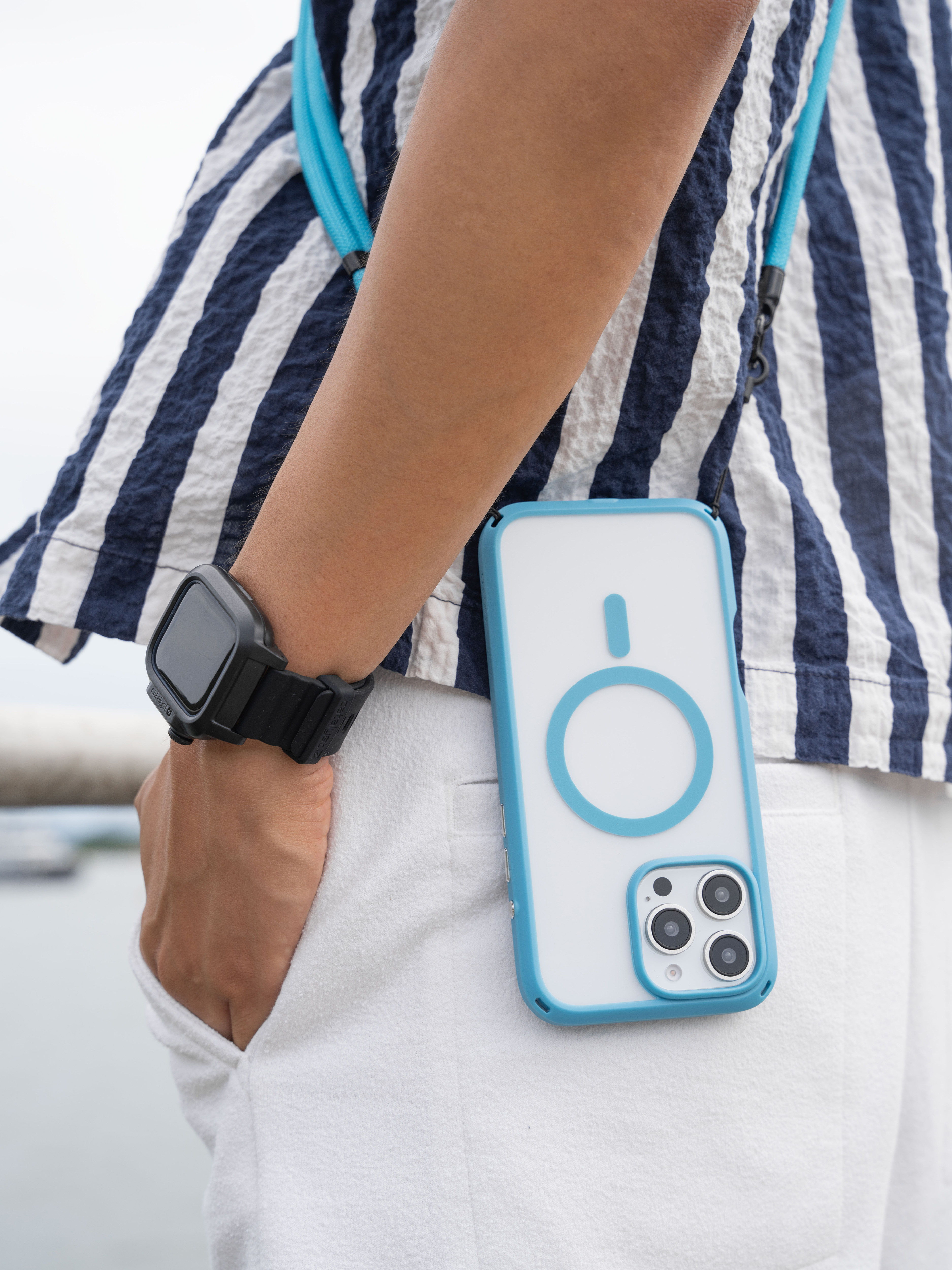 Eine Person im gestreiften Hemd trägt ein blaues Smartphone mit Umhängeband und eine schwarze Armbanduhr.