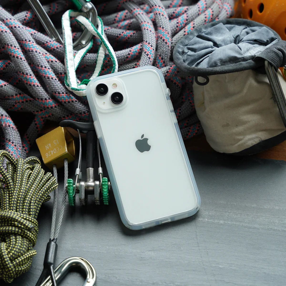 Ein weißes iPhone liegt auf einer dunklen Oberfläche, umgeben von Kletterseilen, Karabinern und einem Chalkbag.