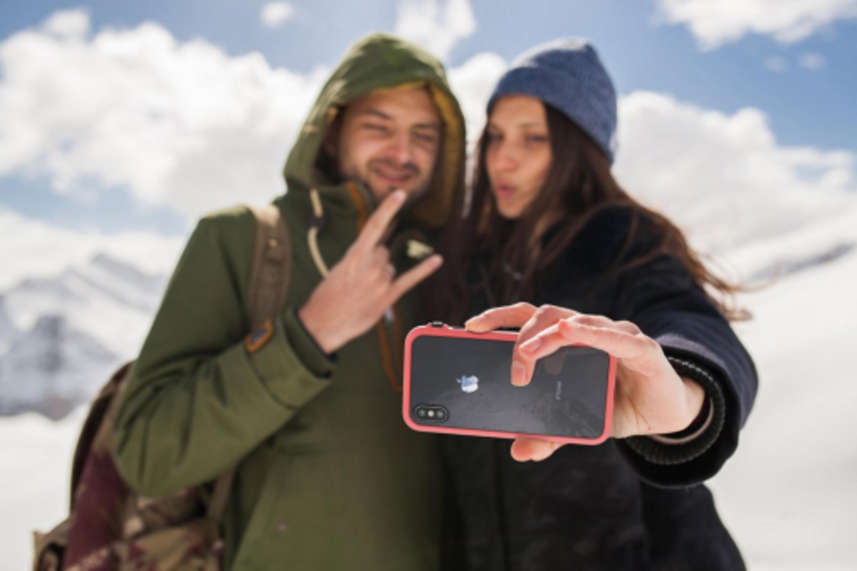 Ein Paar macht ein Selfie in verschneiten Bergen, der Mann macht ein Rock-Zeichen.