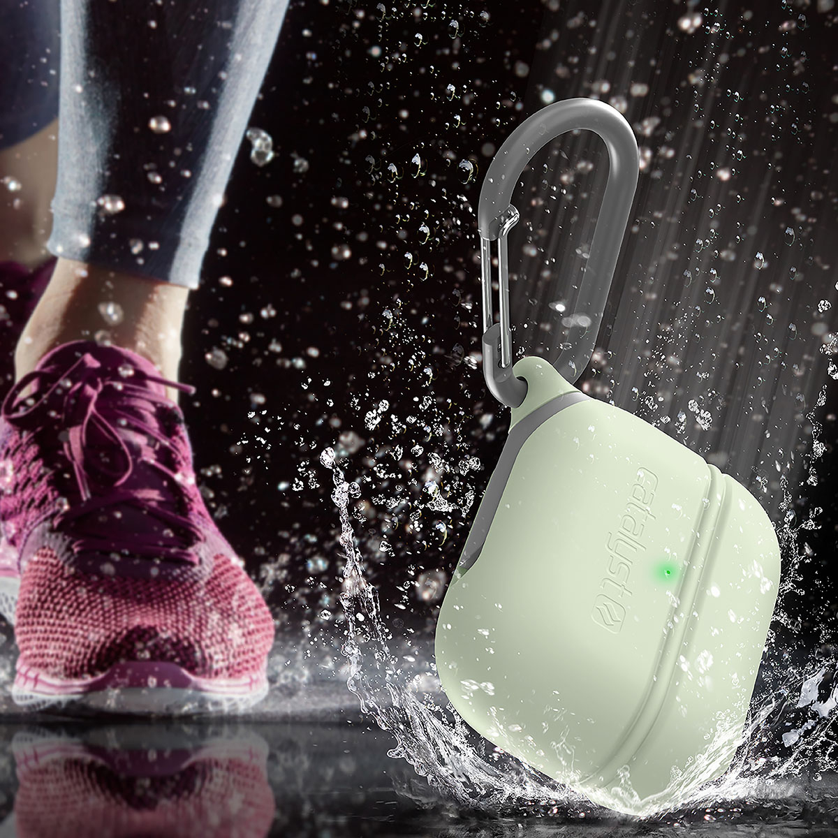 Grüne Kopfhörerhülle mit Karabiner im Wasser neben einem Joggingschuh.