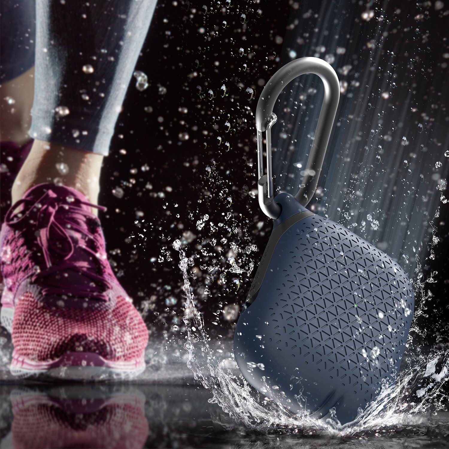 Eine blaue Silikonhülle mit Karabiner steht in spritzendem Wasser neben einem Laufschuh.
